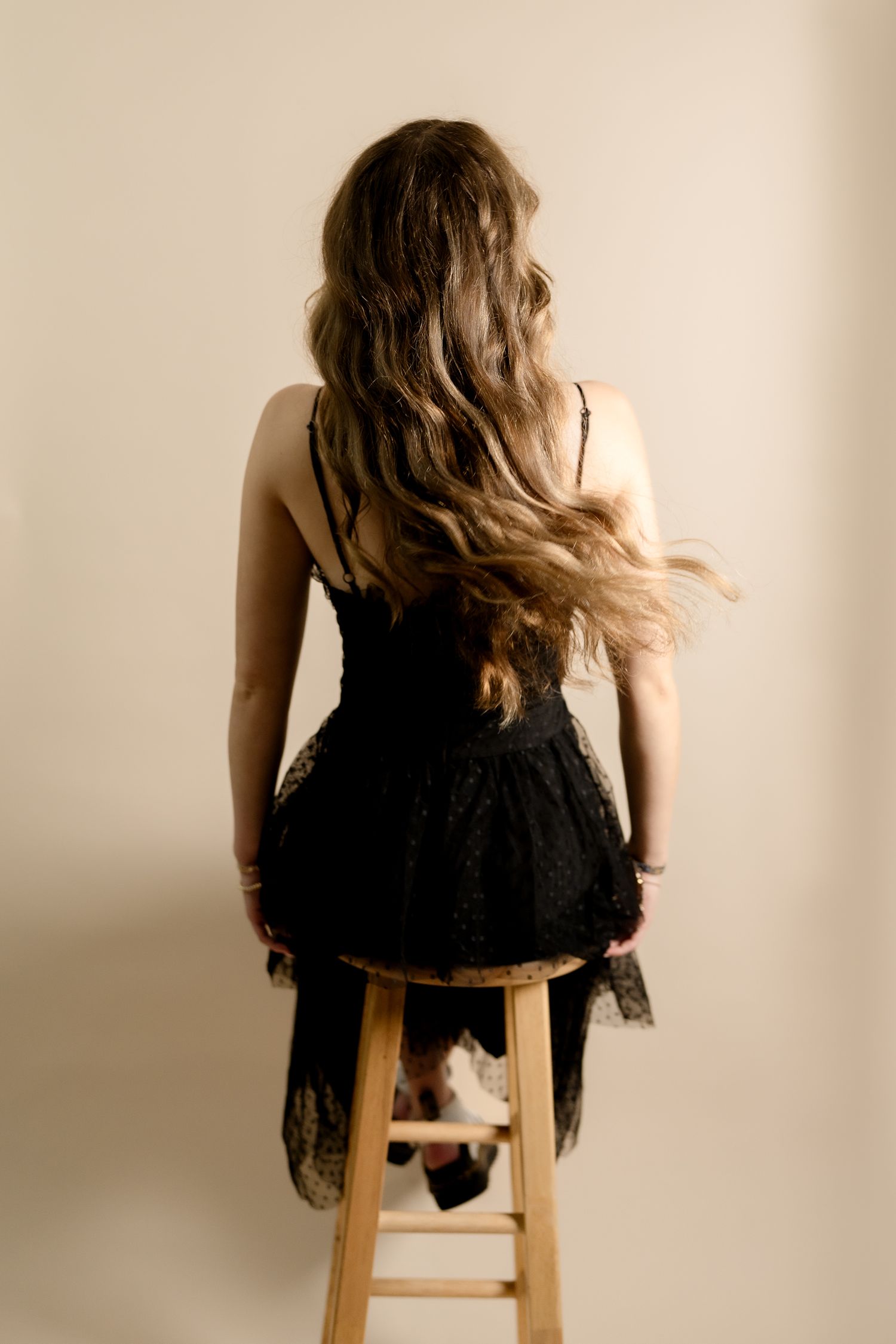 Back view of model in black dress seated on wooden stool.