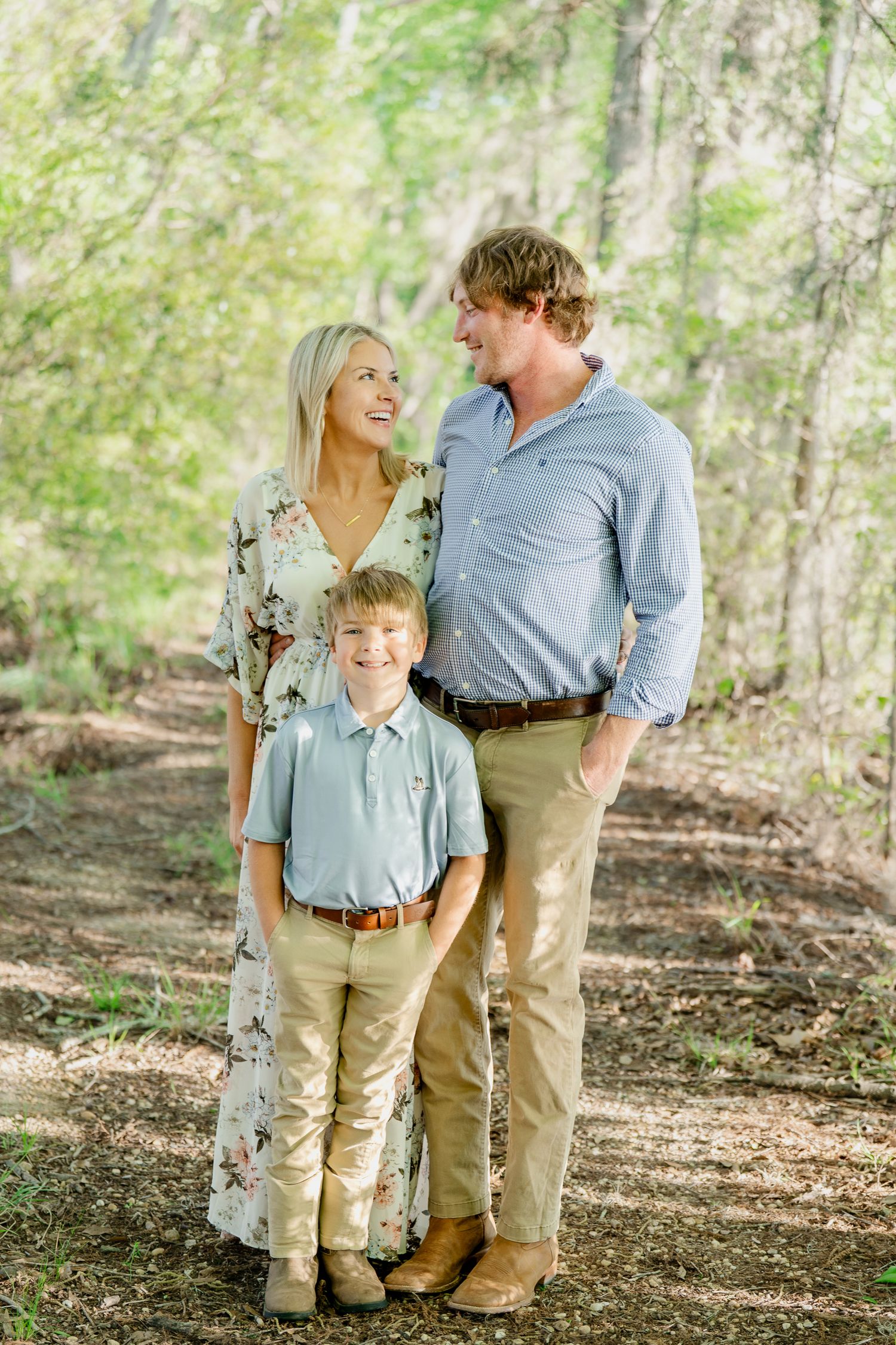 Family wearing coordinated blue and khaki outfits pose together in a wooded setting.
