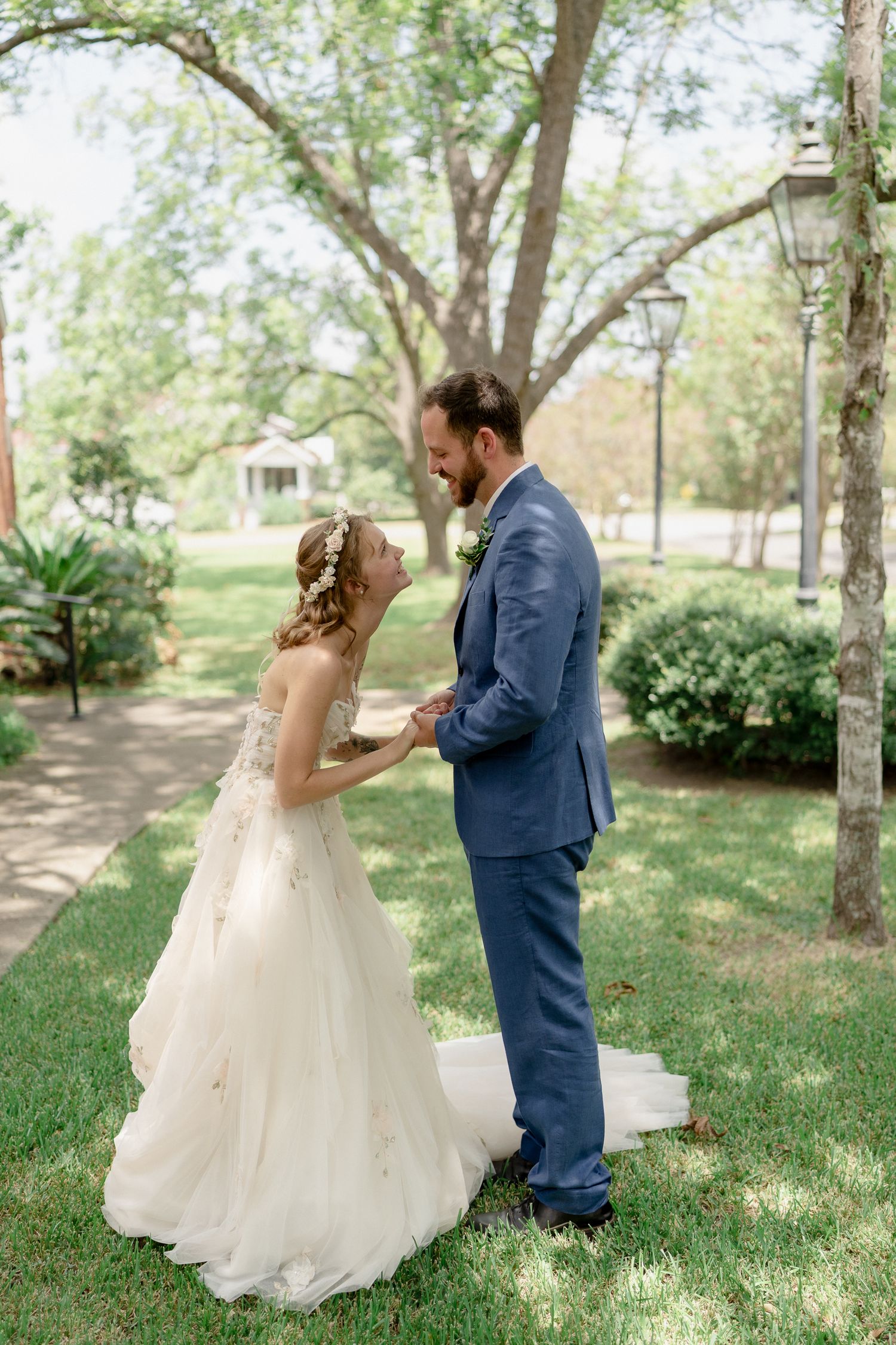 Bride and groom share playful moments during their first look in a sunlit garden setting.