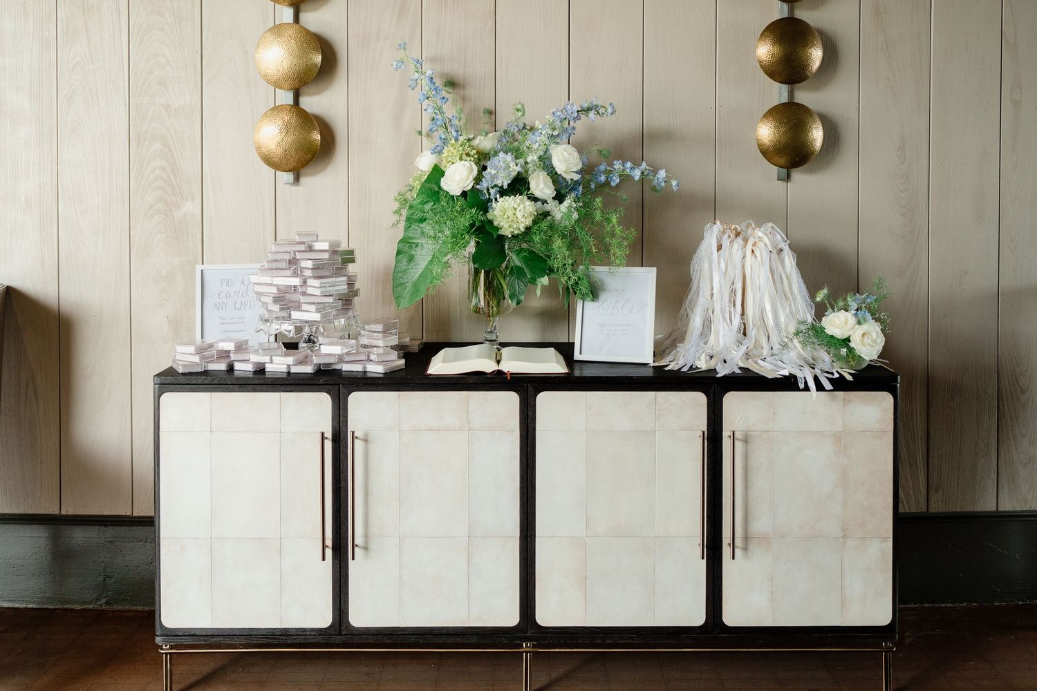 A modern white cabinet with brass spherical pendant lights and floral decor creates an elegant entryway display.