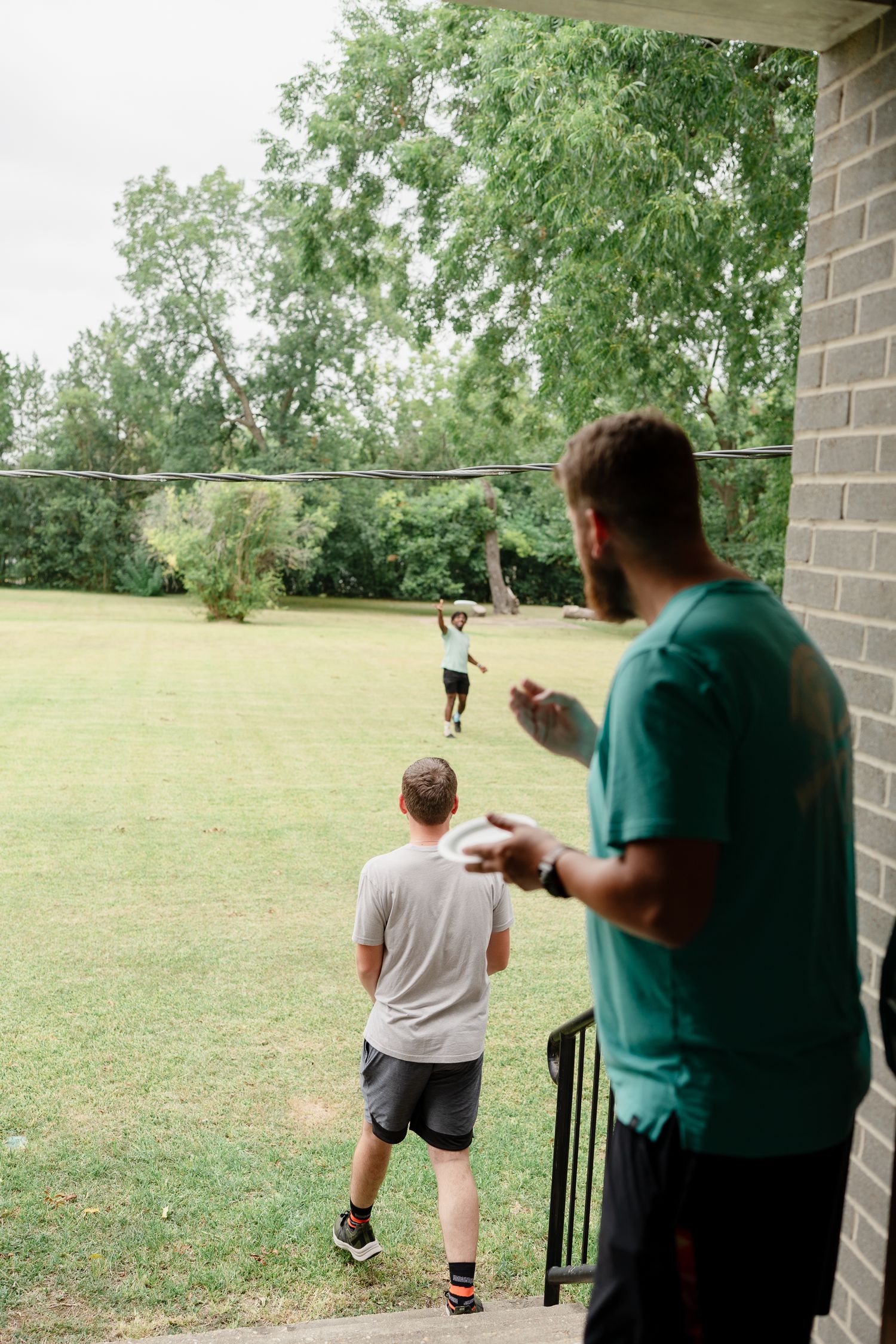 People practicing skeet shooting in a backyard with green trees in the background.