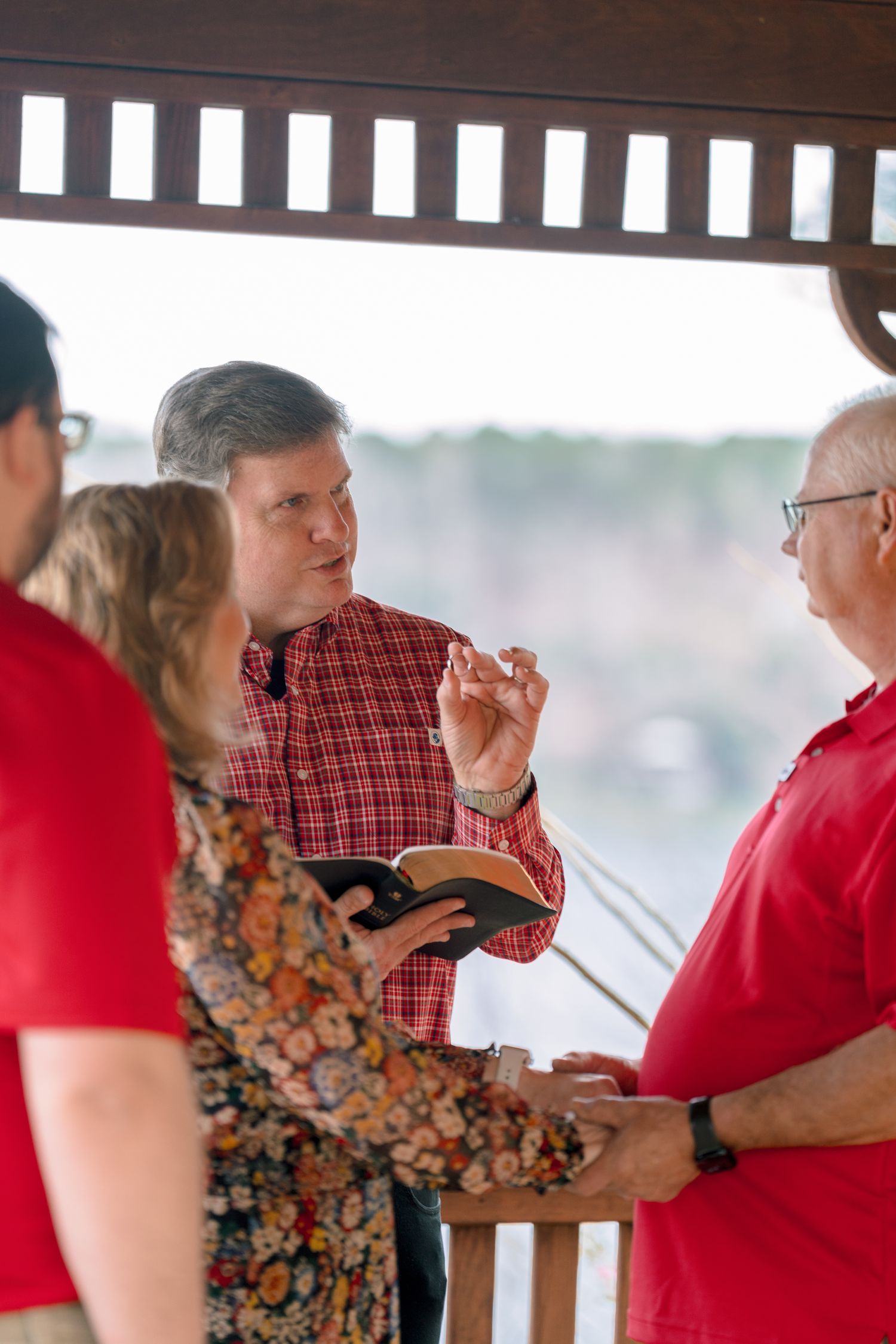 Wedding officiant in plaid shirt reading from Bible during intimate gazebo ceremony.