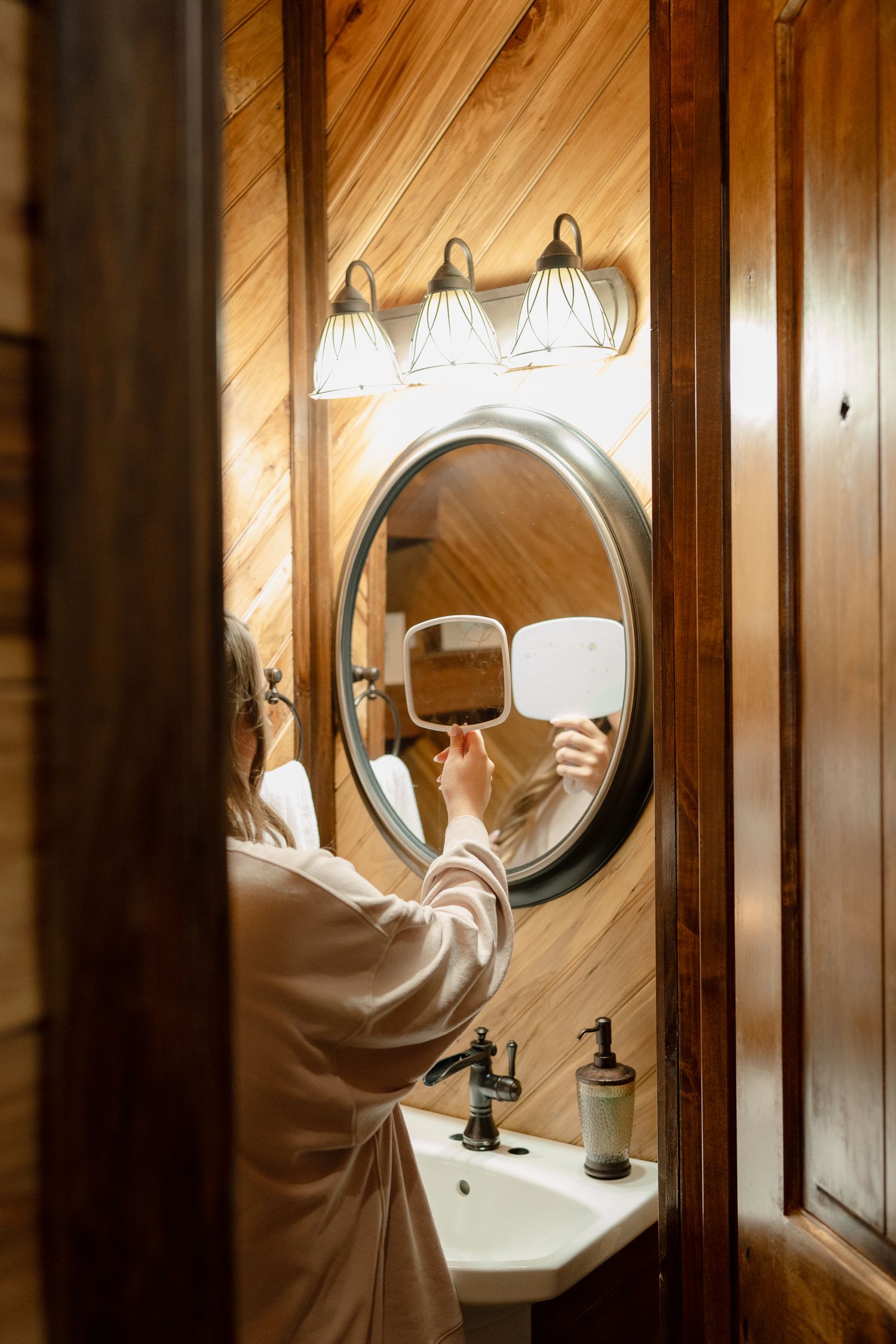 Elegant bathroom interior with curved wooden walls and illuminated oval mirrors creating a warm, luxurious atmosphere.