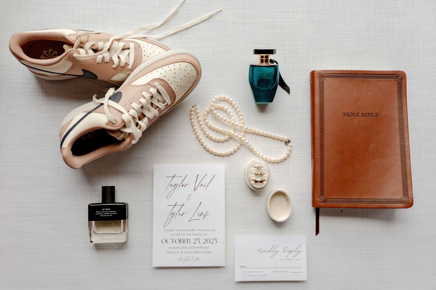 Wedding details flatlay with beige sneakers, perfume bottle, pearl necklace, invitations and brown leather journal.