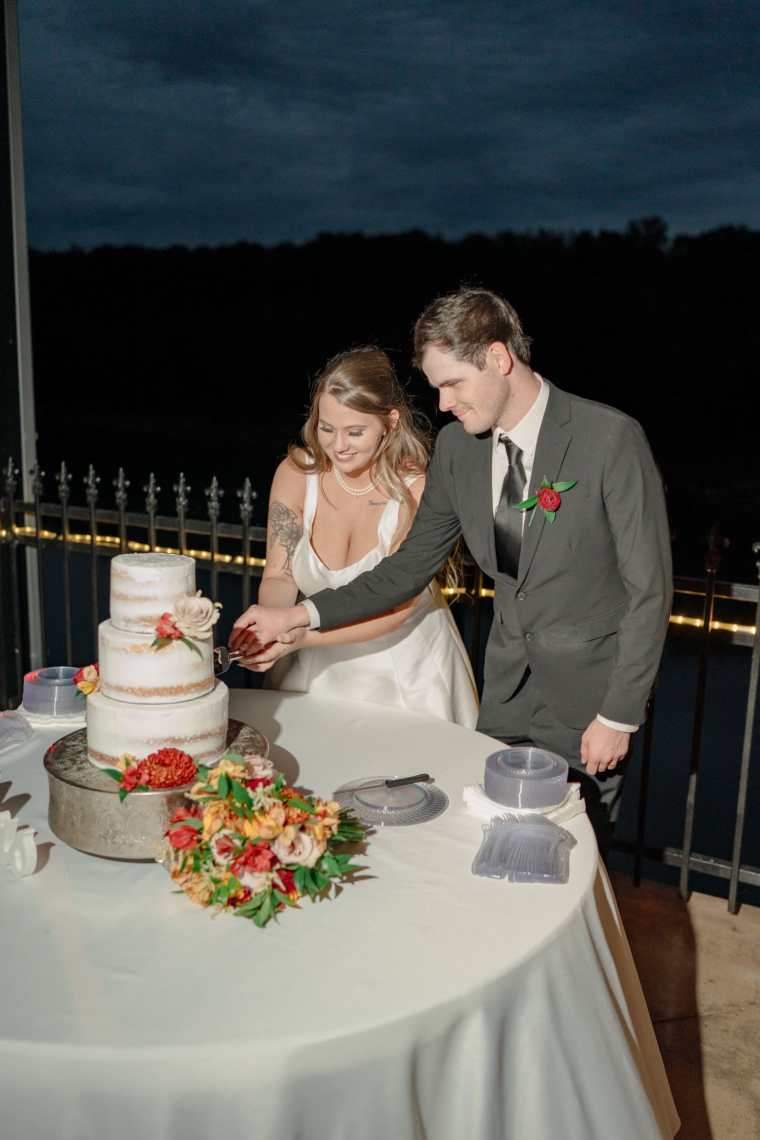 Wedding couple cutting their white tiered cake at reception with floral decorations.