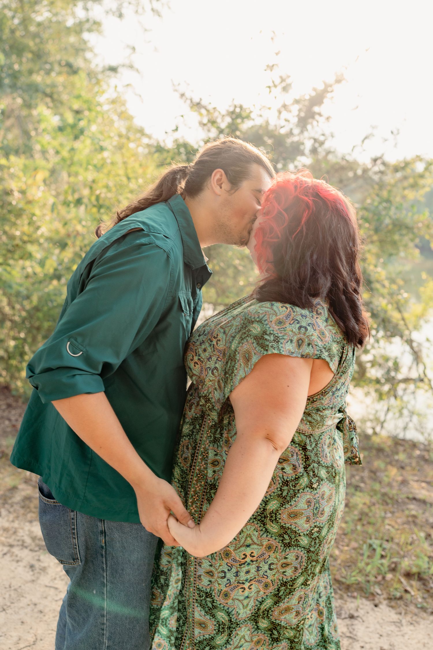 A romantic couple embraces in a natural outdoor setting with soft sunlight filtering through trees.