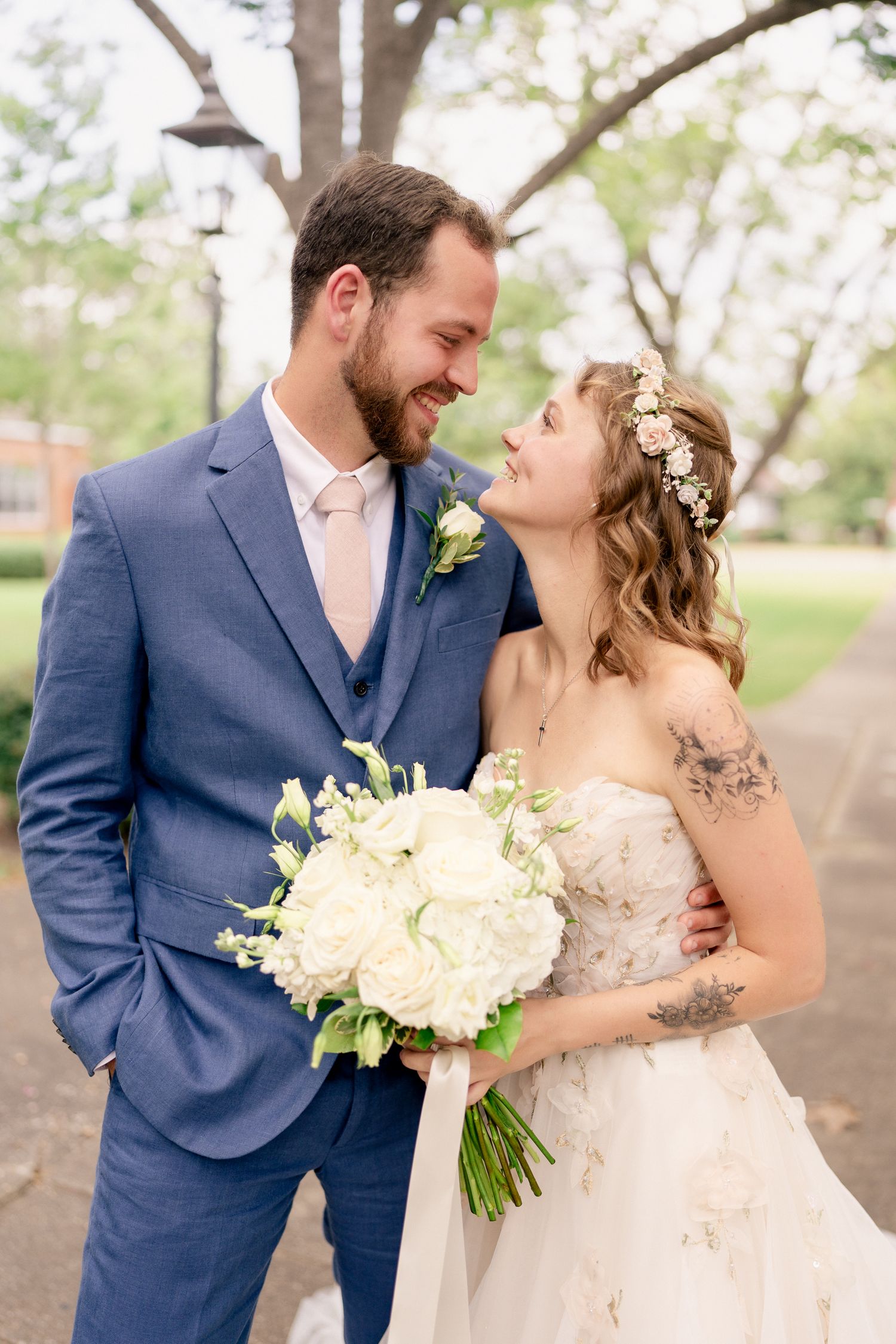 A romantic wedding couple shares a tender moment in a garden setting with the bride holding a white floral bouquet.