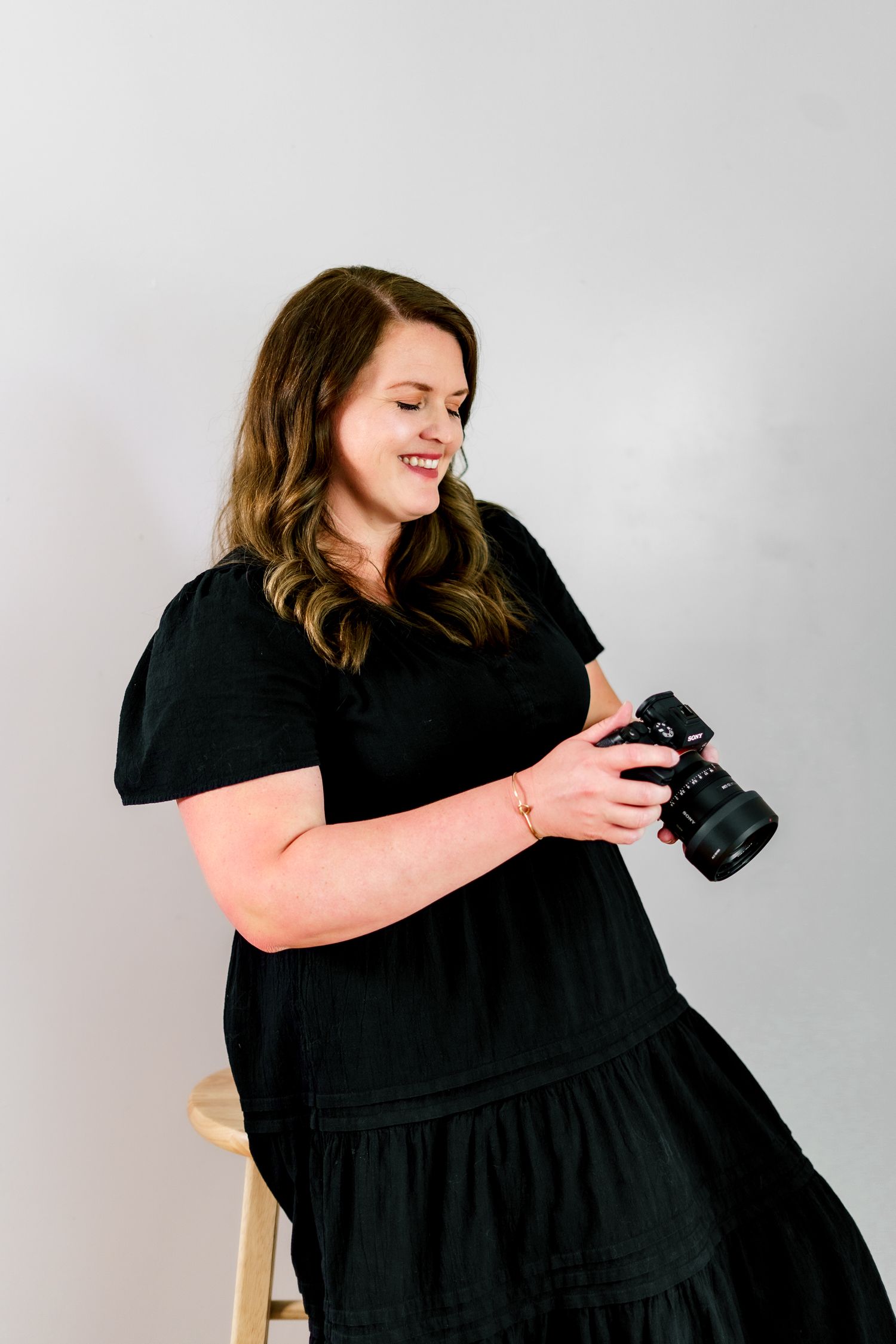 A photographer in a black dress demonstrates different camera holding positions during a shoot.