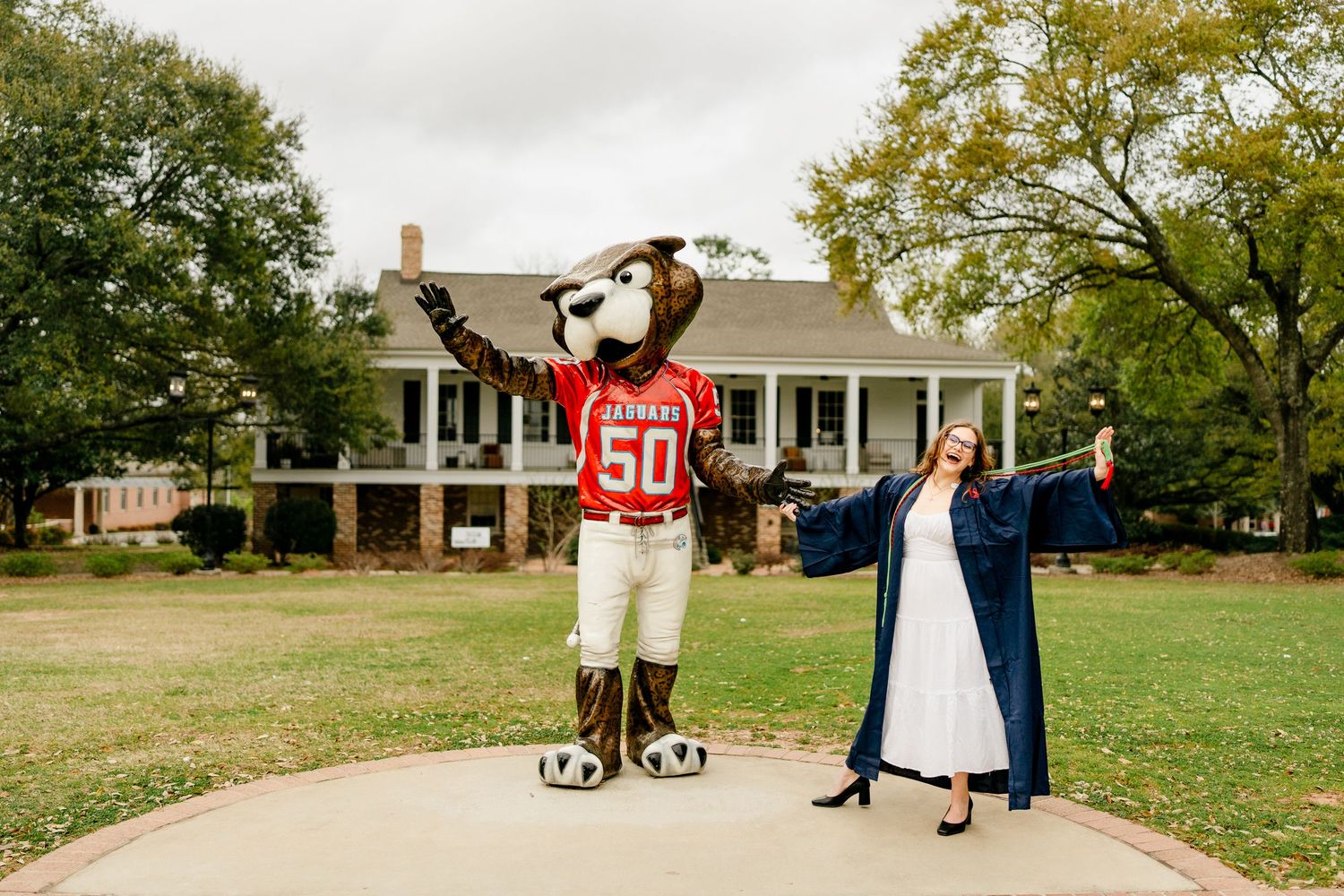 Graduate and mascot pose together on campus walkway during graduation photoshoot.