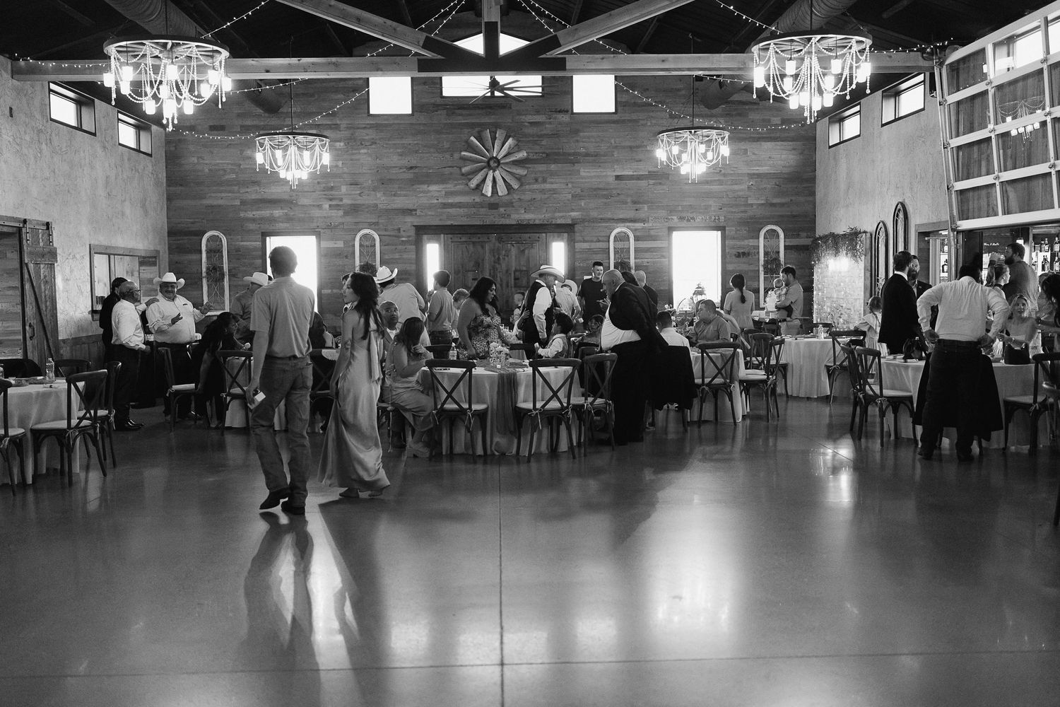 Black and white photo of wedding reception guests mingling in elegant rustic barn venue.