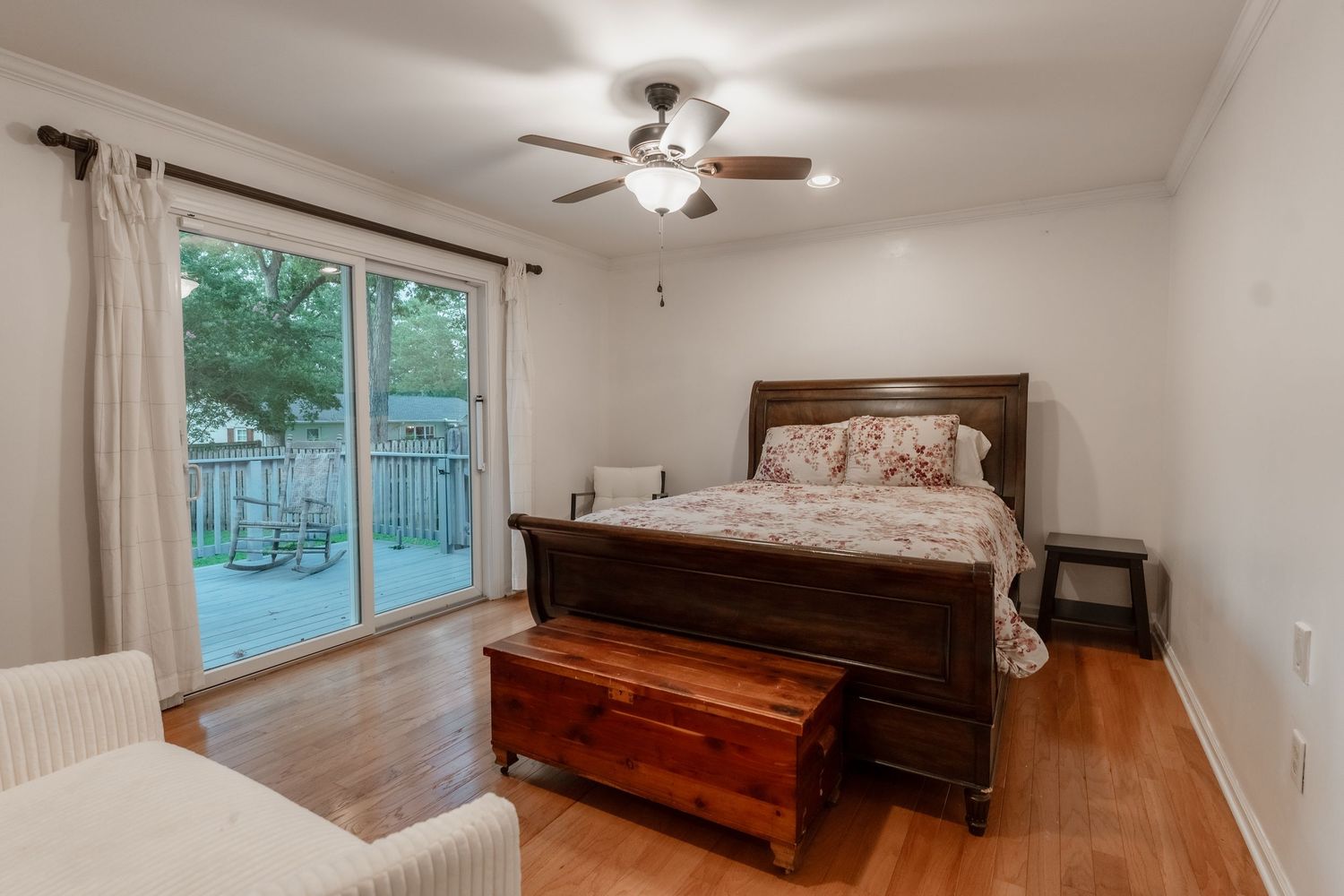 Panoramic view of a bright bedroom with hardwood floors, ceiling fan, and large windows overlooking trees.