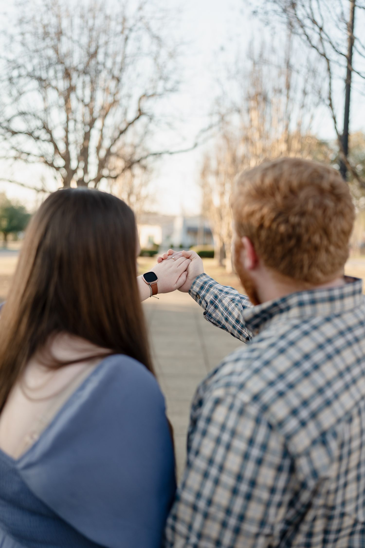 Couple holding hands outdoors in a park during golden hour, viewed from behind.