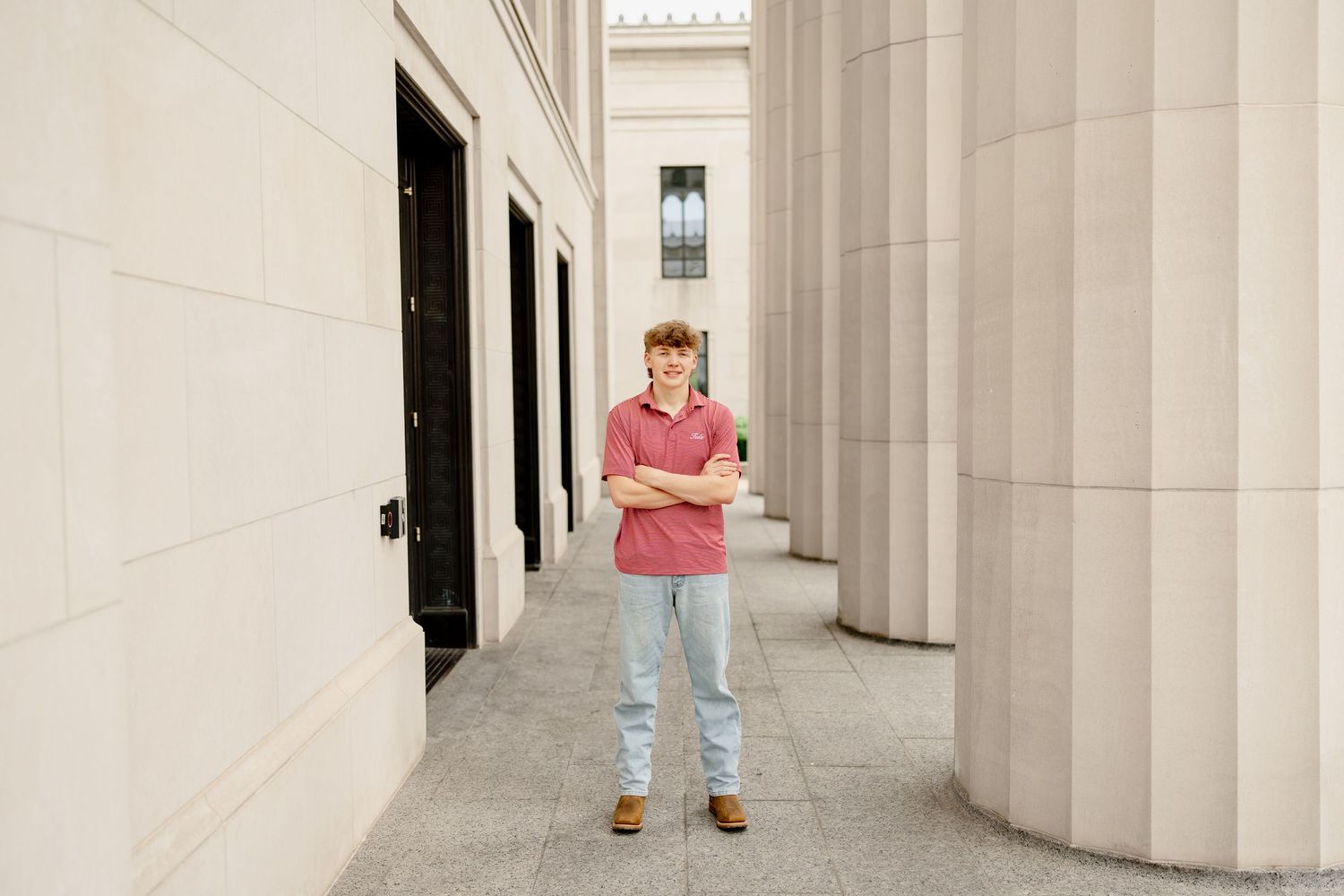 Standing pose between tall white columns in classical building hallway.