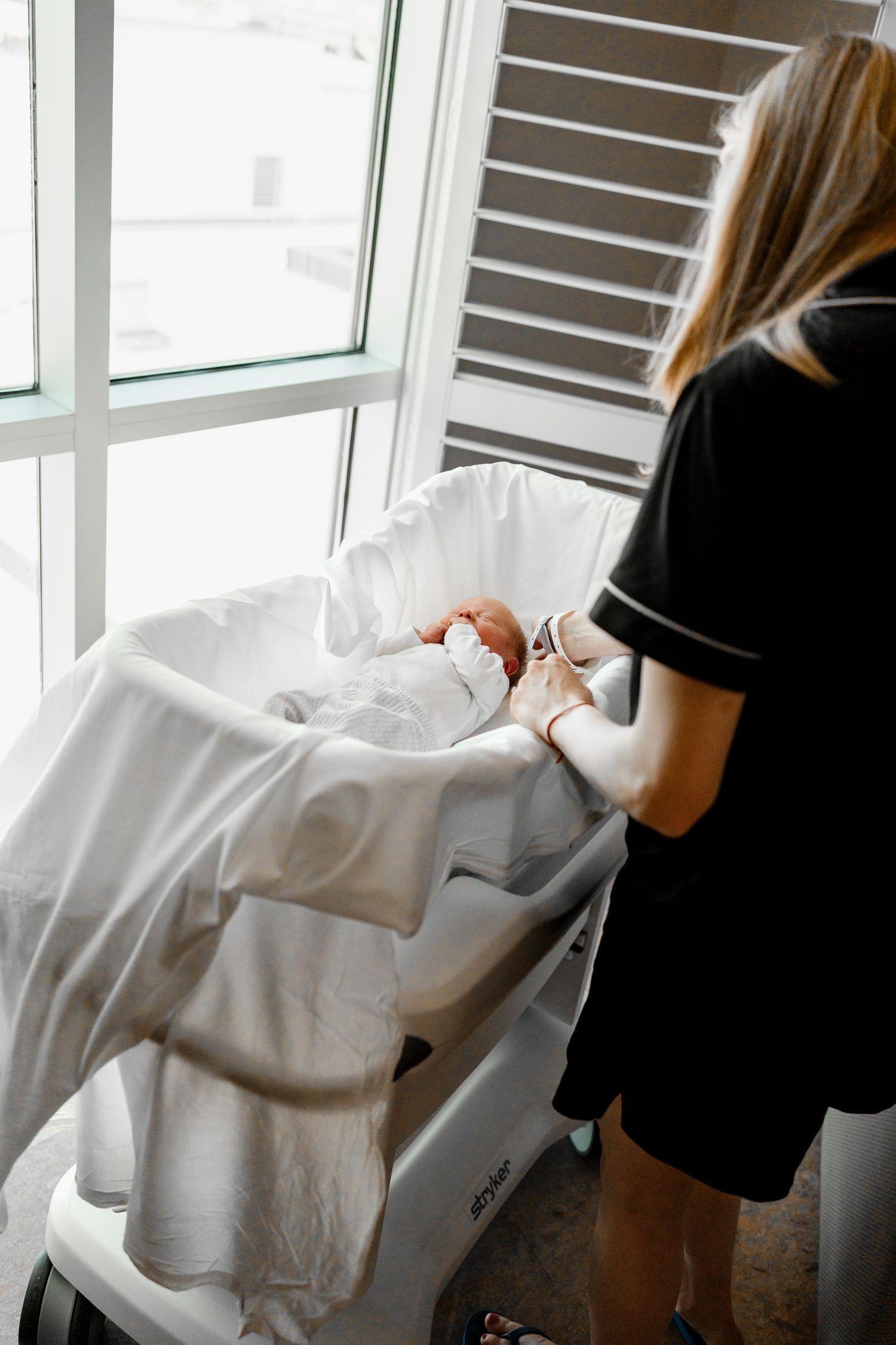 Newborn baby resting peacefully in white bassinet by window.