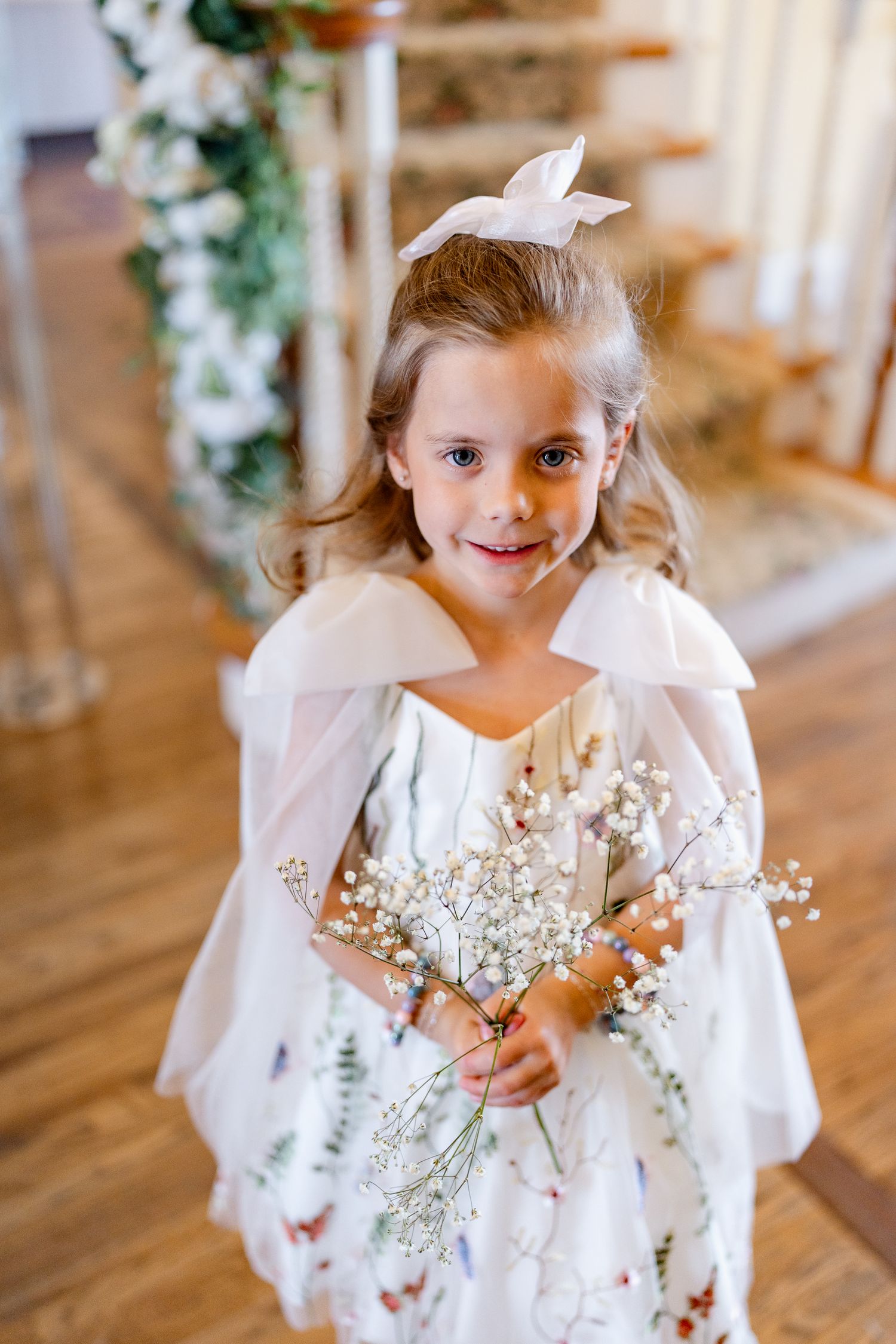 Young flower girl in a white dress with butterfly details holds baby's breath flowers at a wedding.