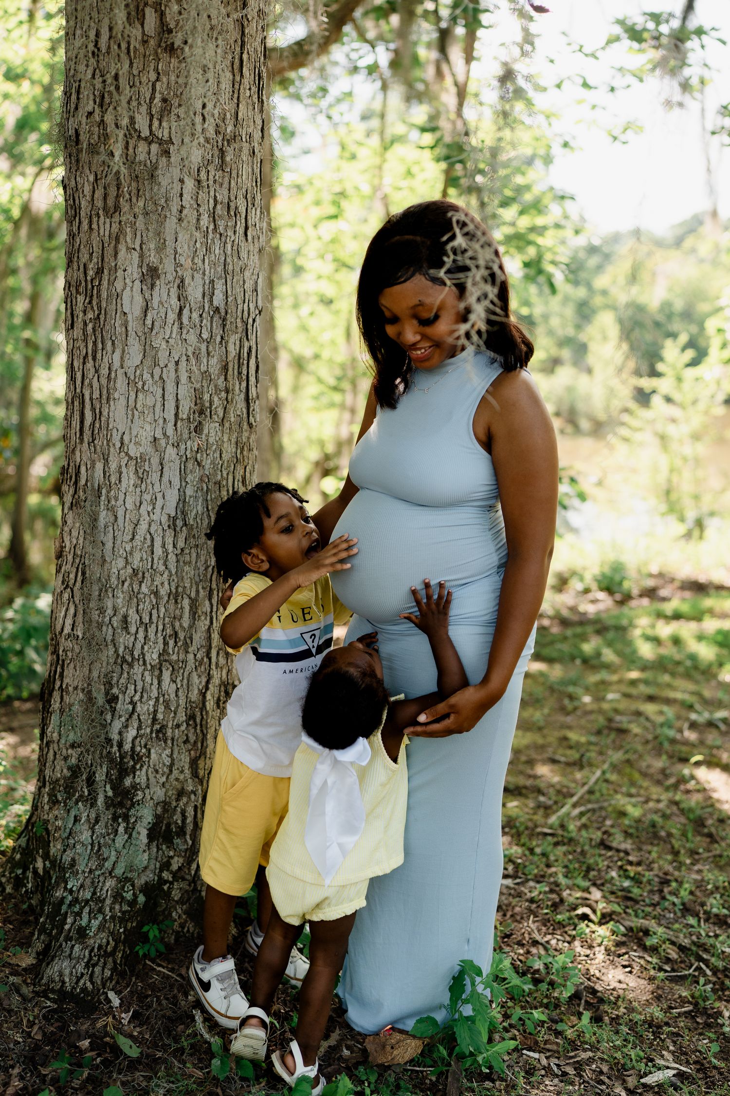 Mother and child share tender moment outdoors in natural wooded setting.