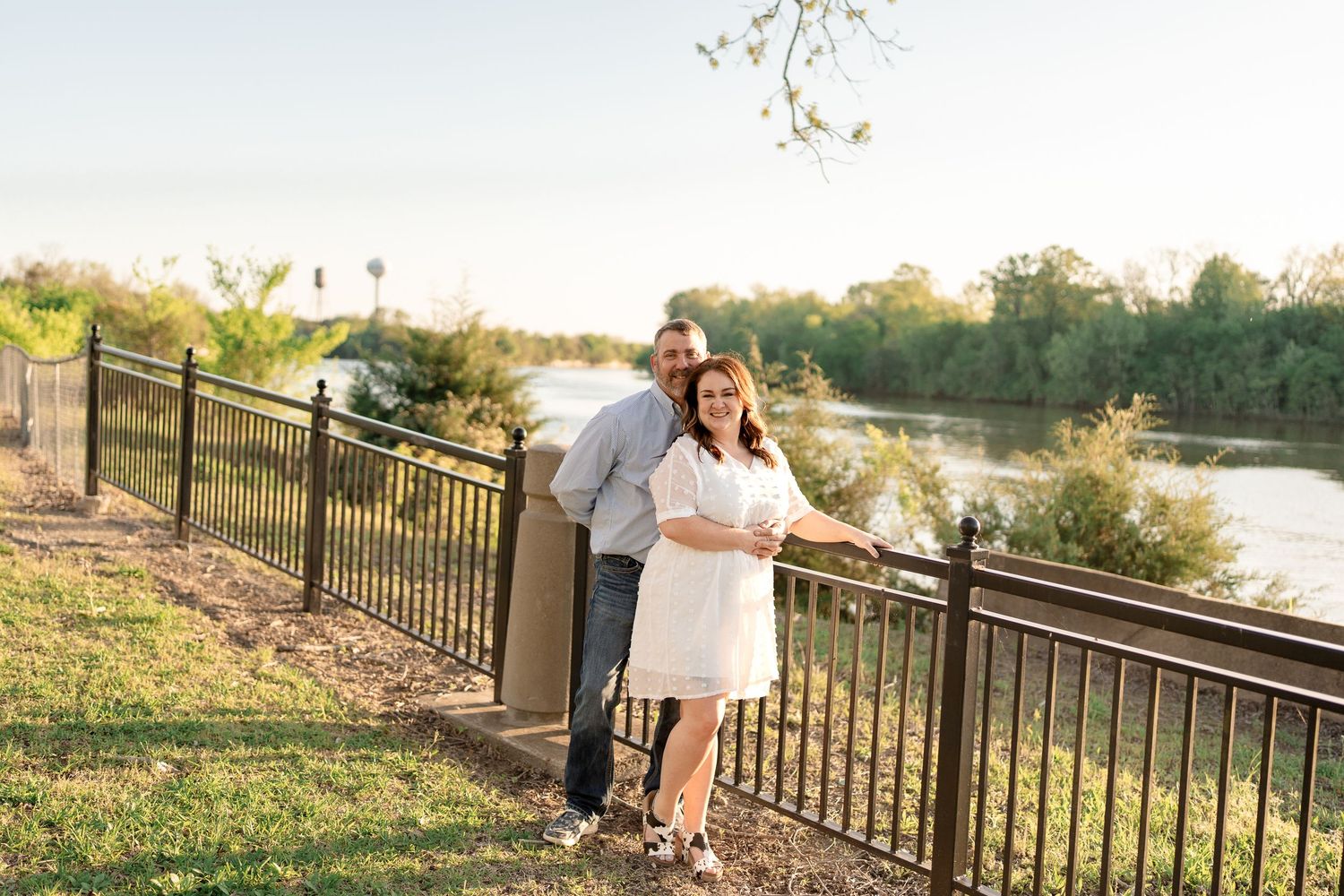 A couple sharing an intimate moment along a riverside railing during sunset.
