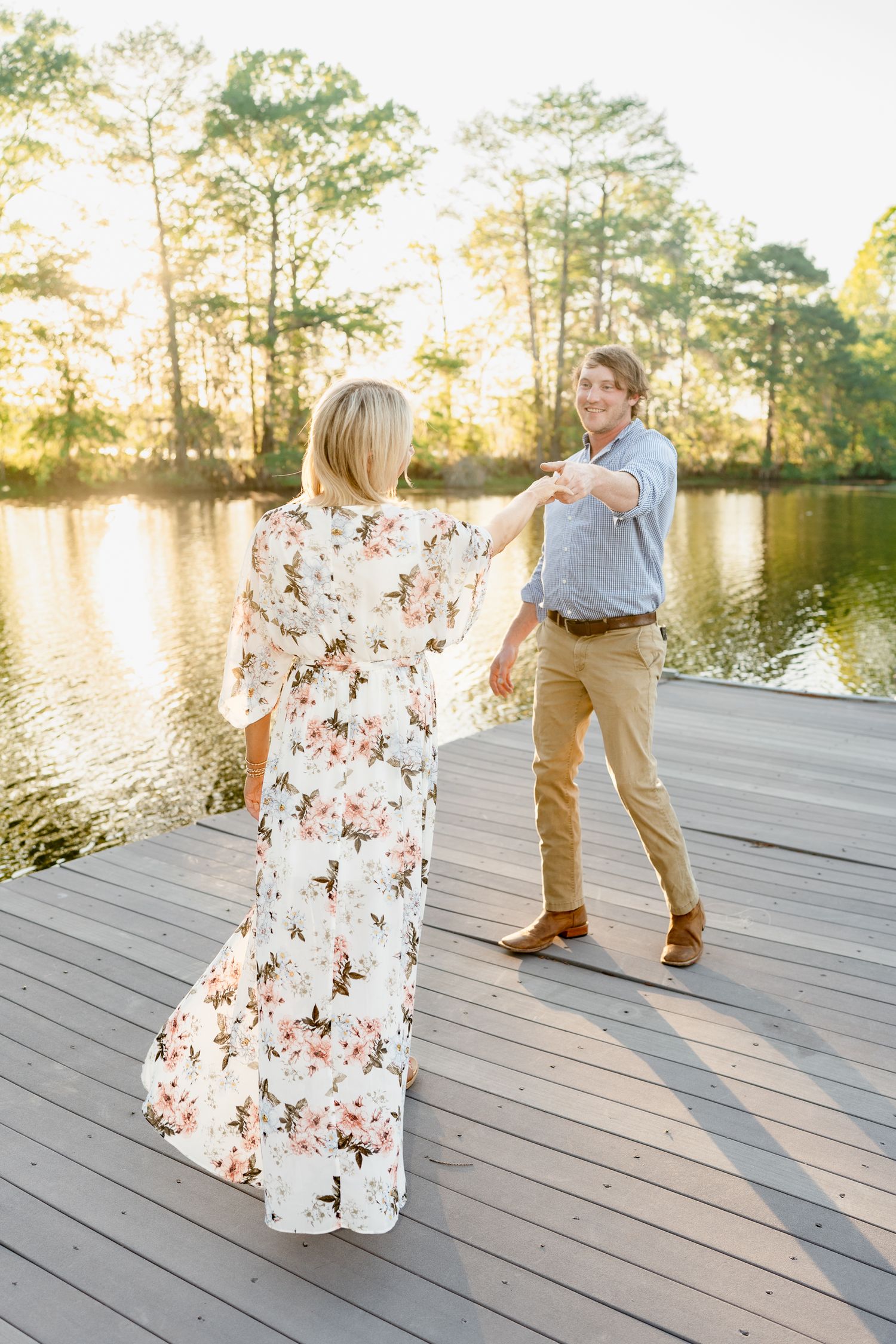 A couple dances playfully on a lakeside dock during golden hour.
