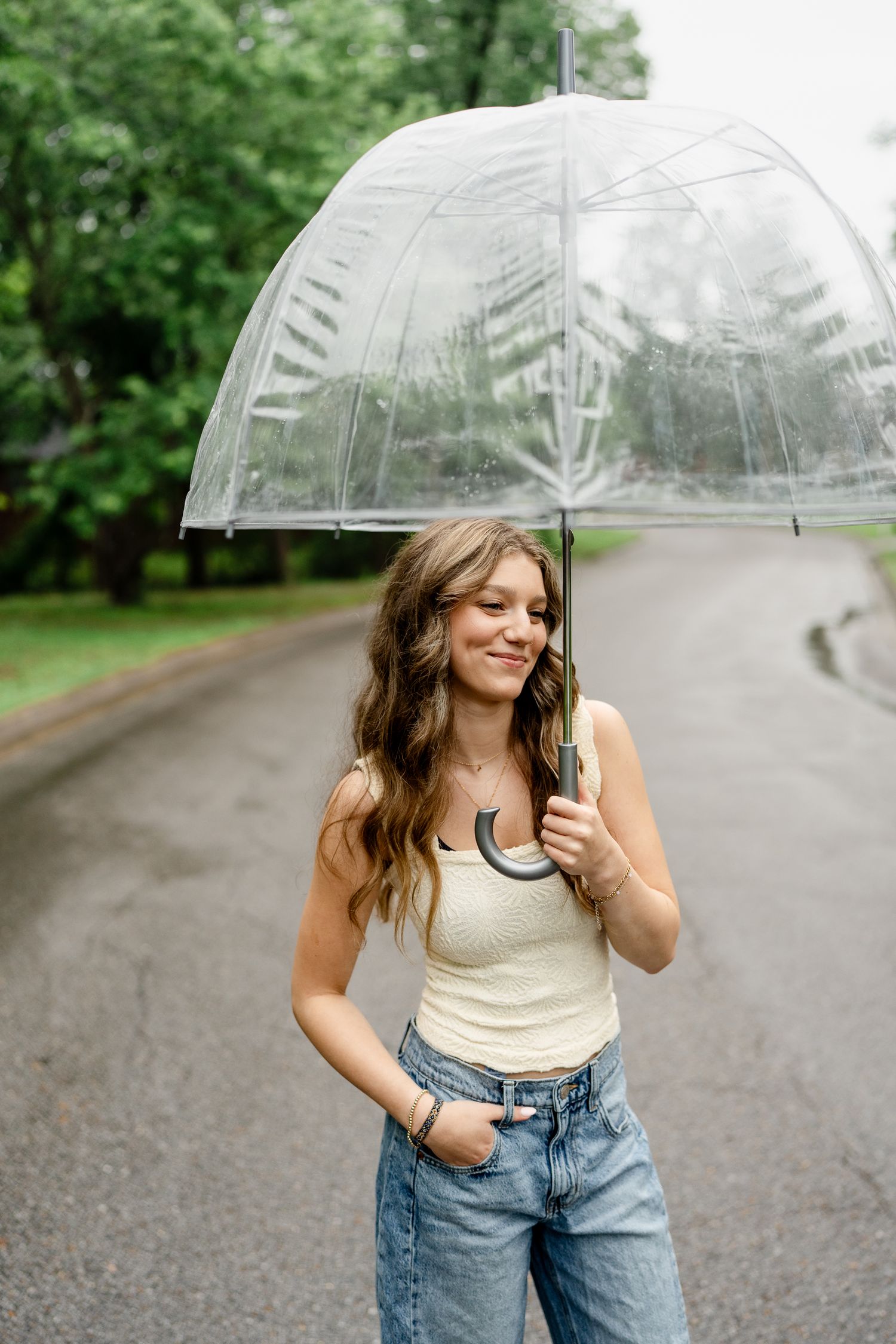 Person holding clear umbrella on rainy day wearing casual summer outfit.