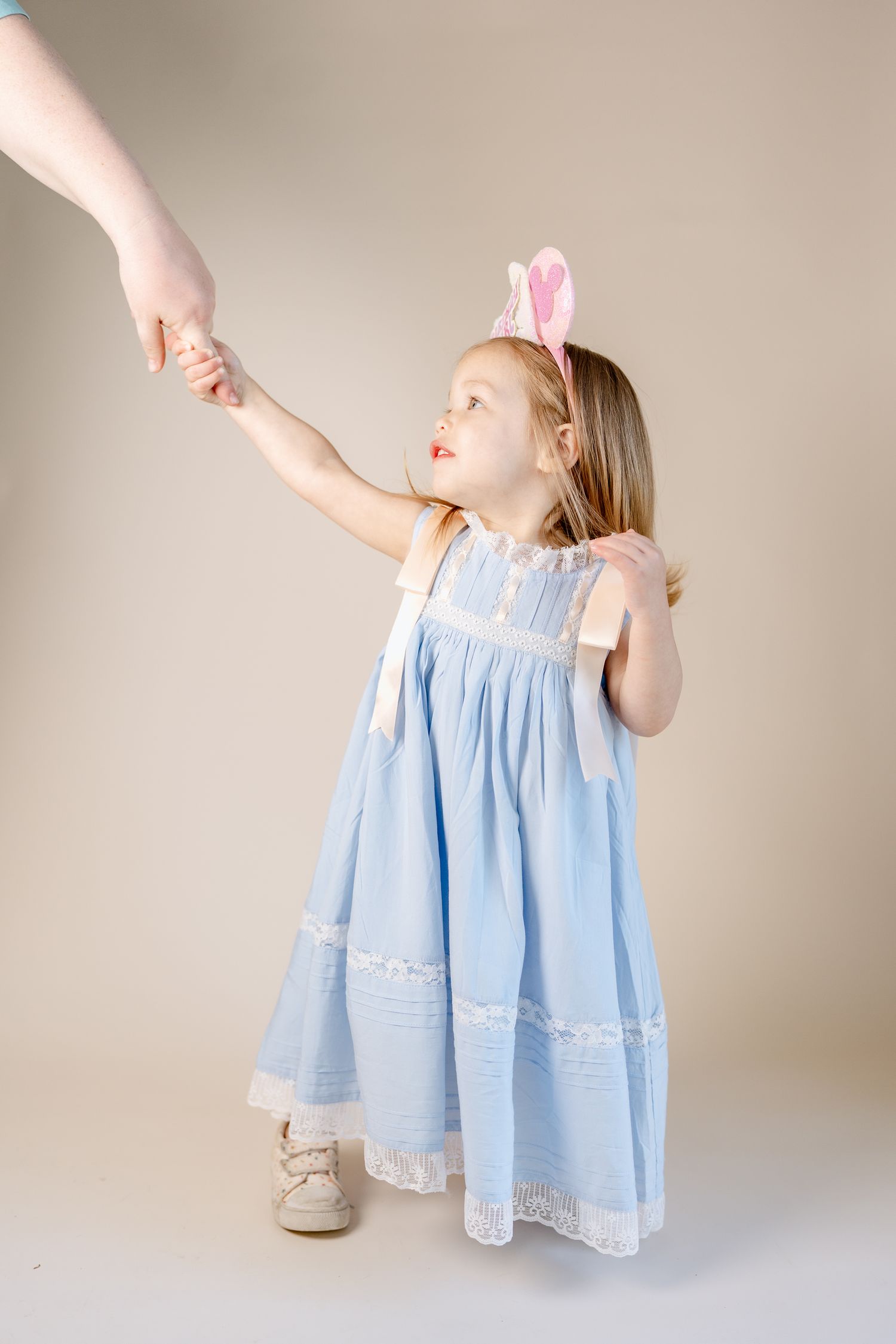 A light blue dress with lace details flows elegantly against a beige background.