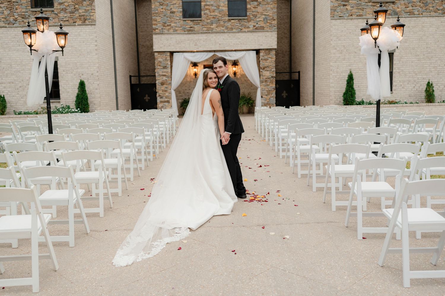 Outdoor wedding venue with white folding chairs set up for ceremony against stone and brick walls.