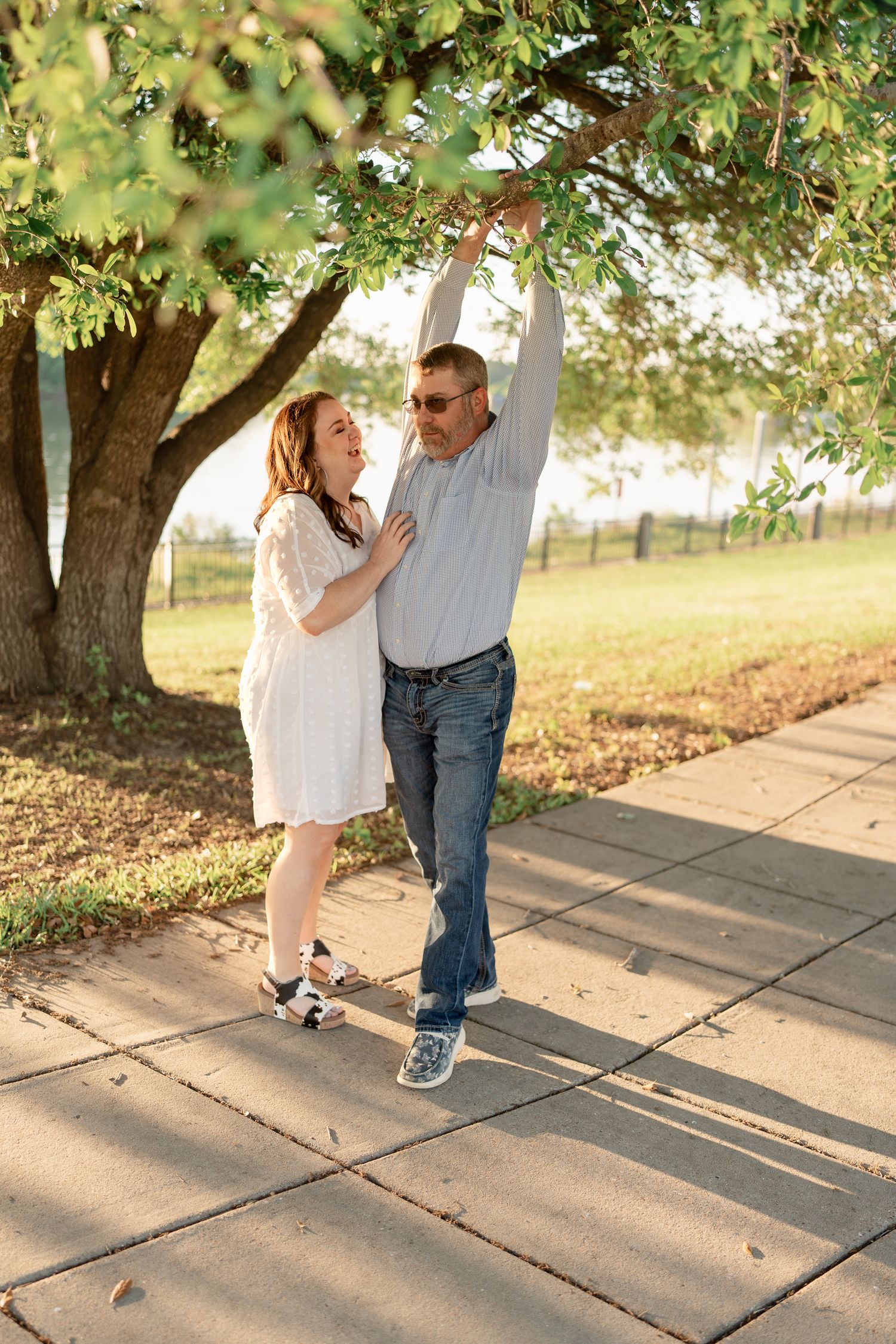 A playful moment between a couple dancing on a path under tree branches.