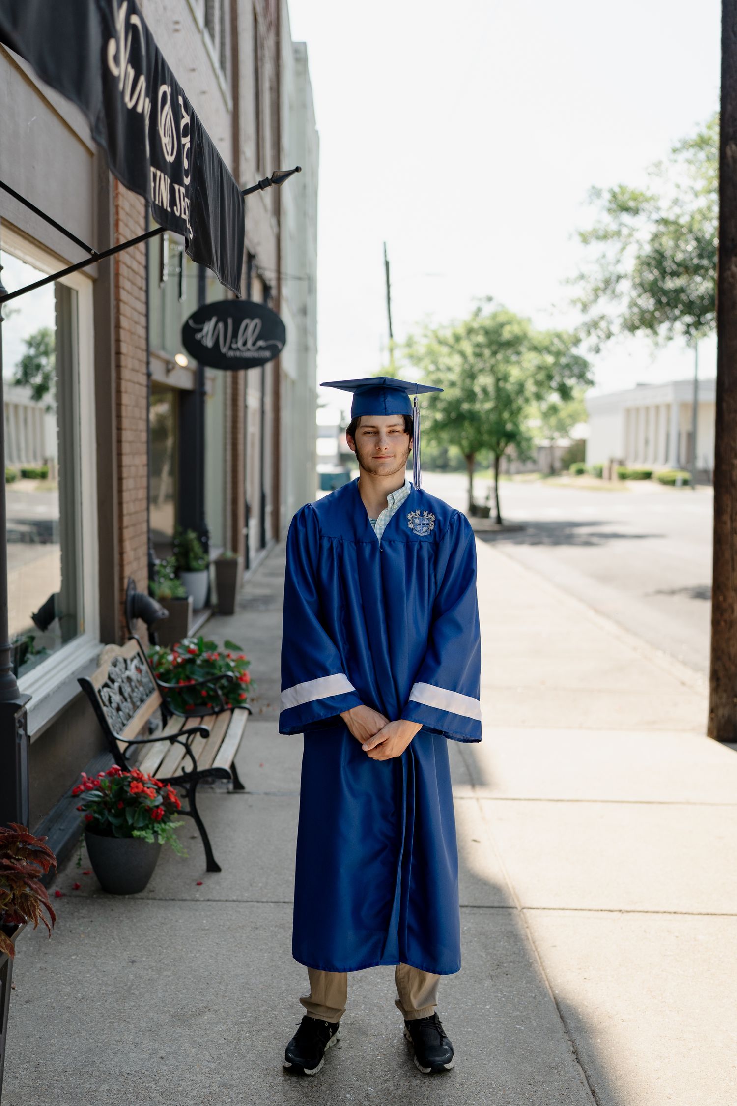 Graduate in traditional blue graduation attire stands on downtown sidewalk.
