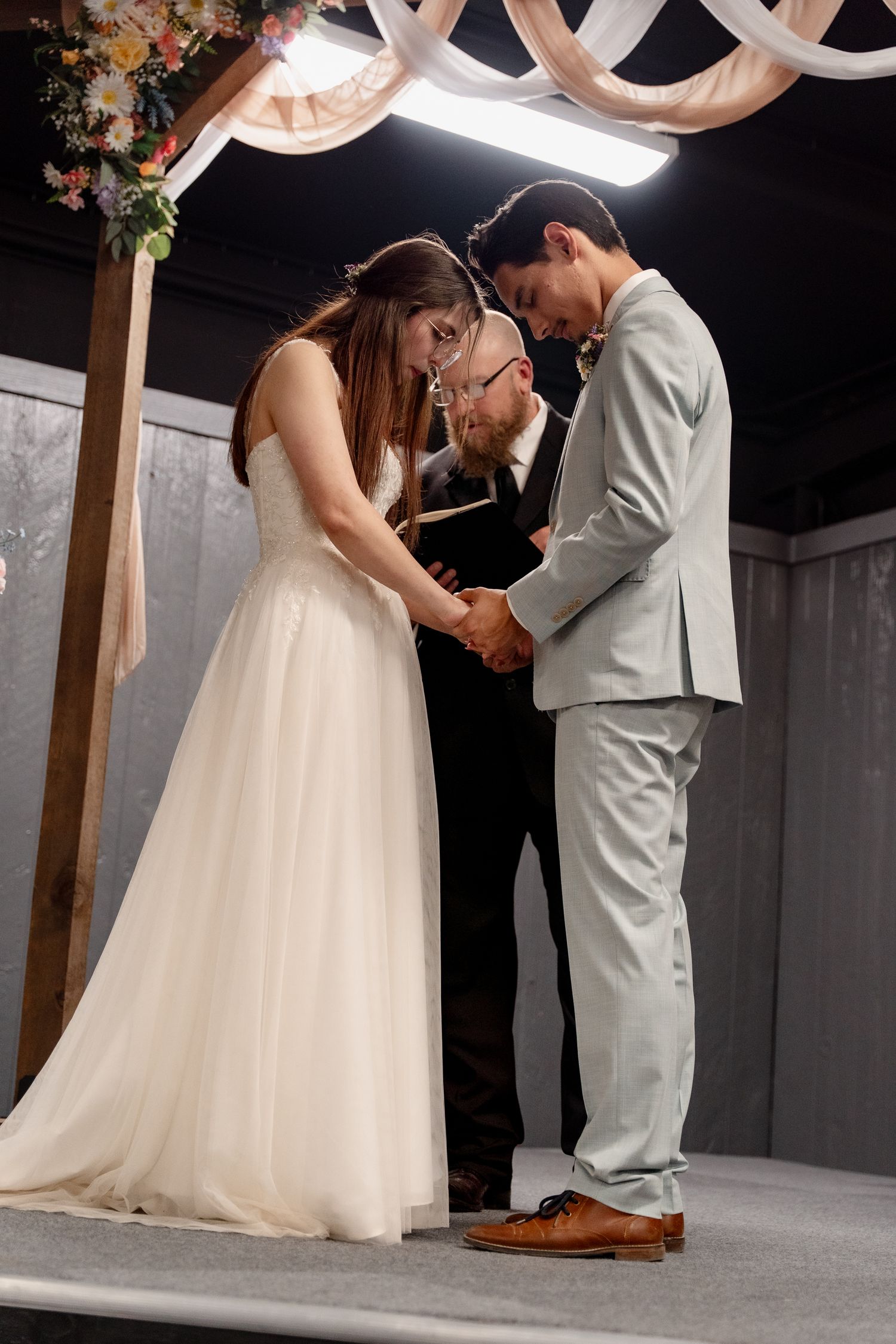 A wedding ceremony taking place under draped fabric and floral decorations with a couple and officiant at the altar.