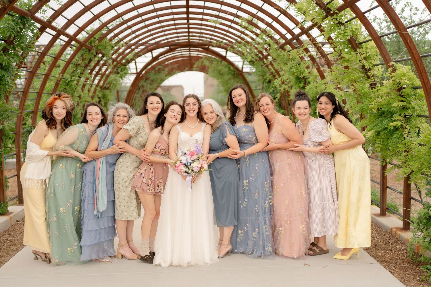 Wedding party in coordinated blue and blush dresses poses together in a garden setting.