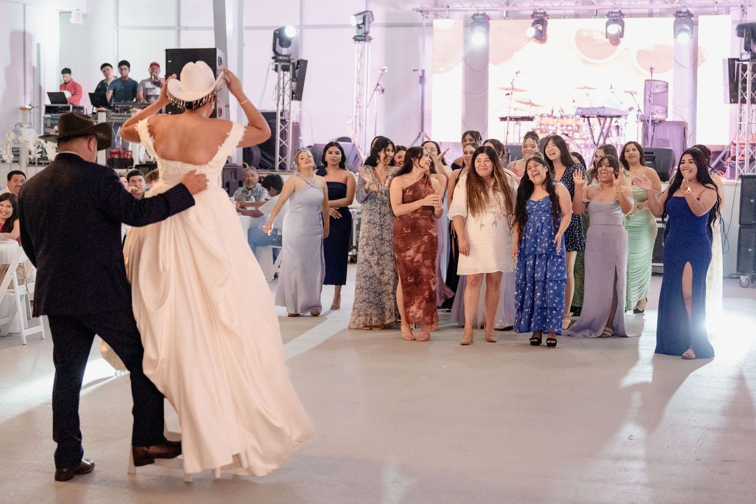 Wedding guests dance together in an elegant white-decorated reception hall during a celebration.