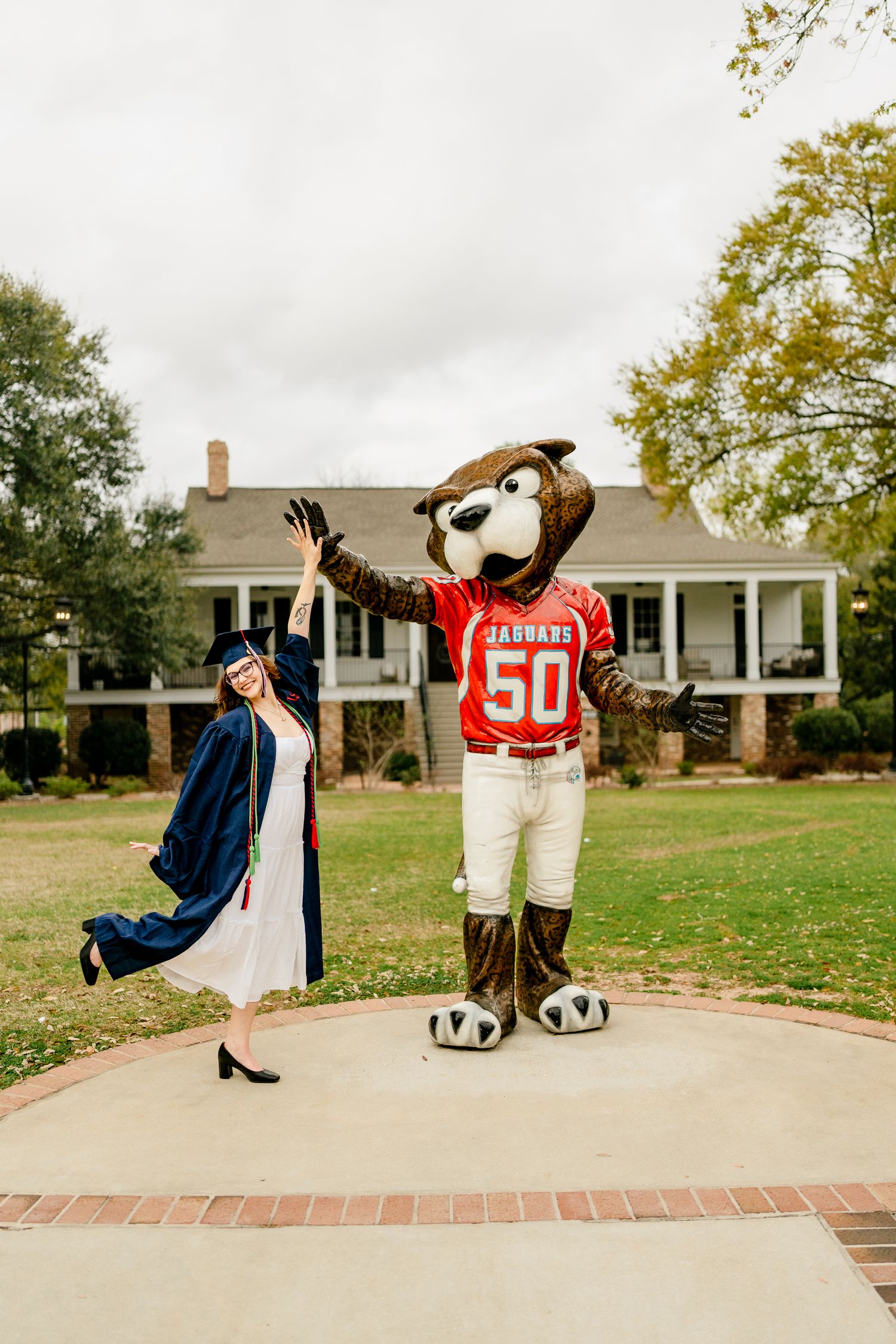Celebratory graduation photo with mascot in front of campus building.