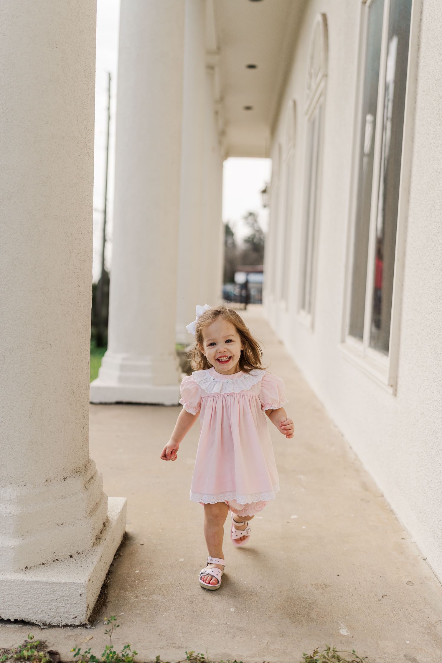 A child runs happily down a covered walkway in a pink dress.