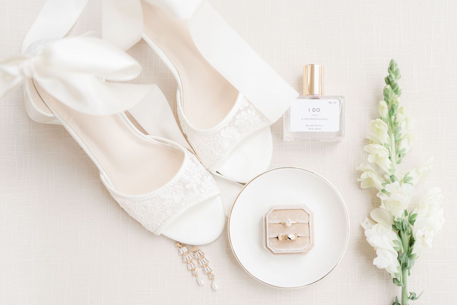 Bridal details flatlay with white ballet shoes, perfume bottle and ring box.