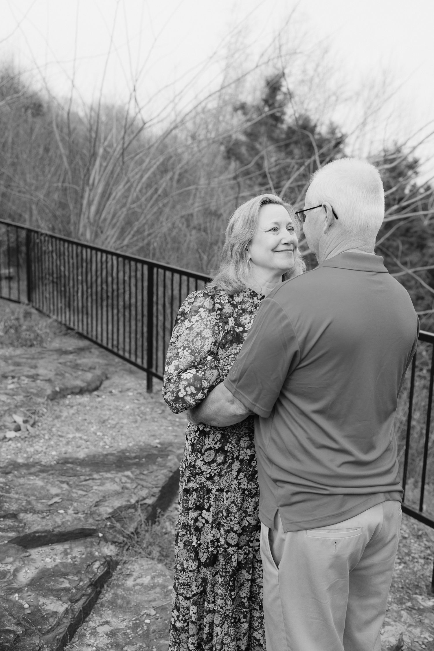 Smiling woman gazes at her partner while standing together near an outdoor railing.