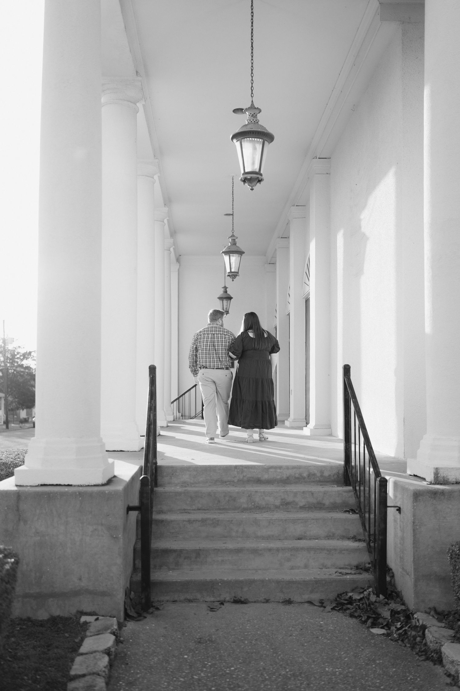Couple walking along a classic columned corridor with hanging lanterns, black and white photo.