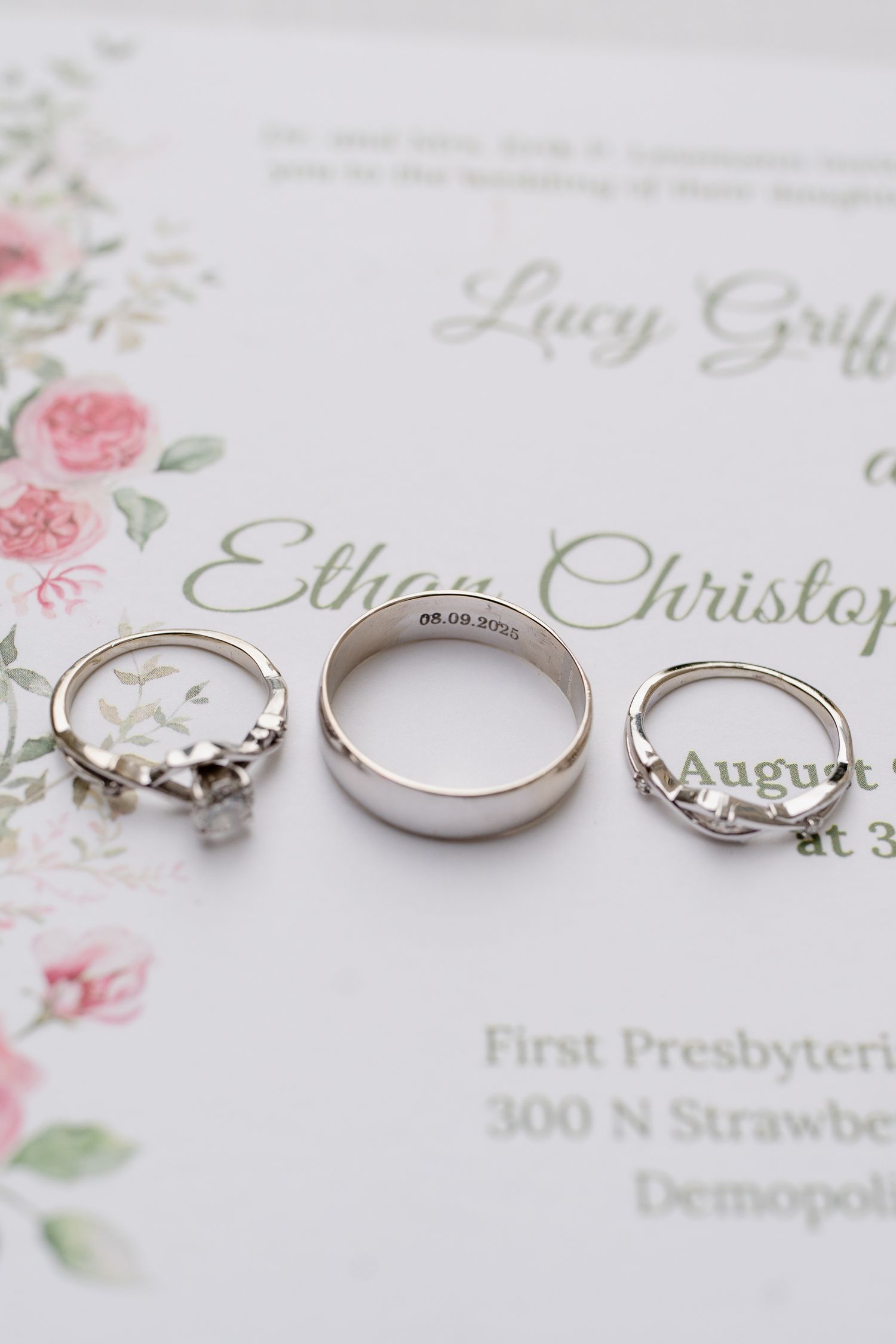Wedding rings and engagement ring displayed on floral wedding invitation with delicate pink roses.