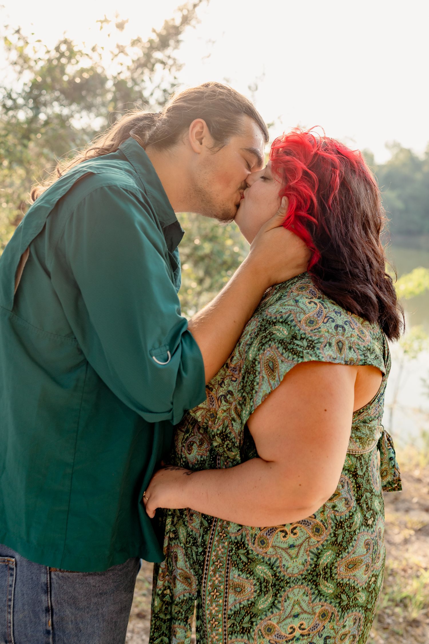 A romantic couple sharing a tender kiss outdoors during golden hour in a natural setting.