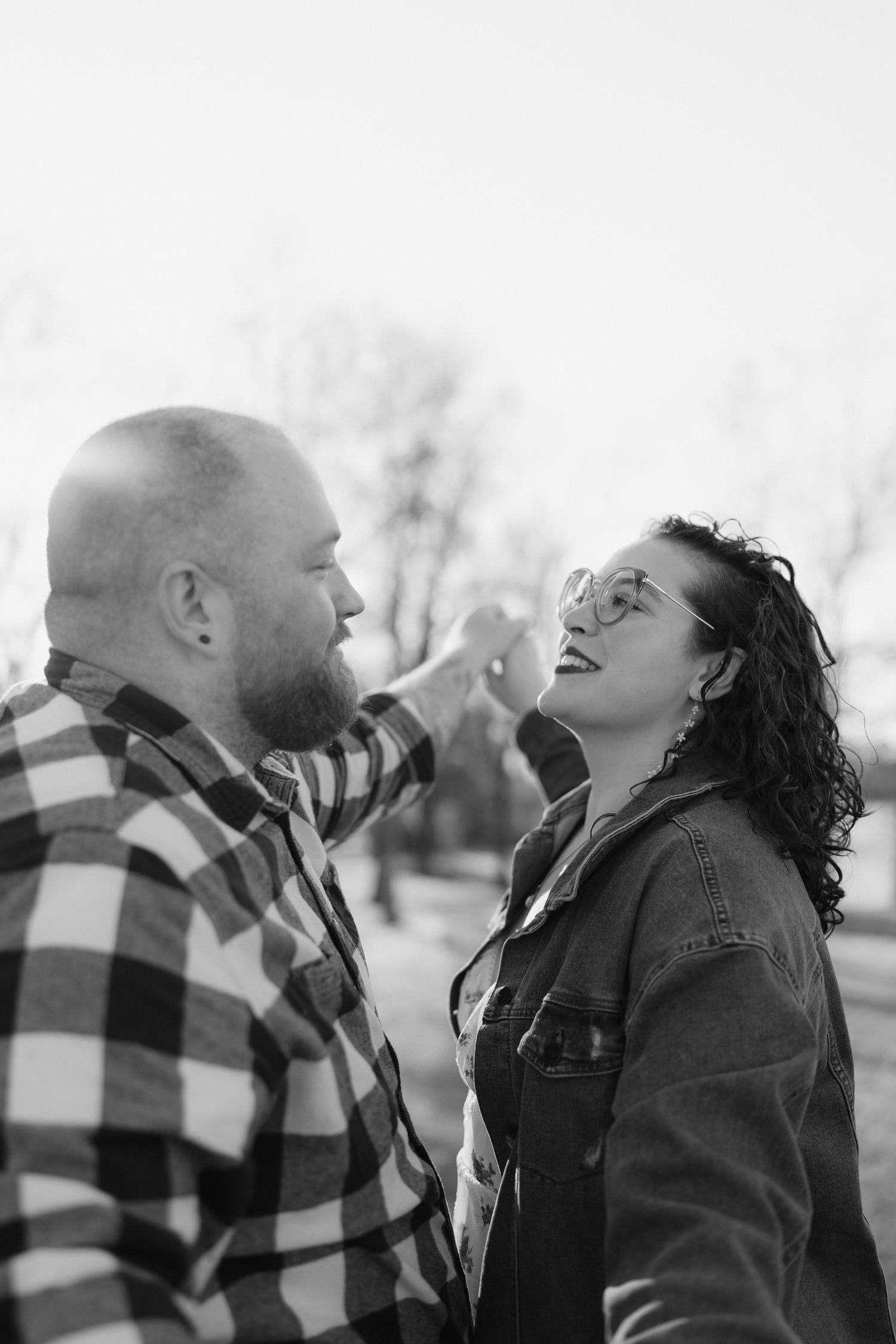 A couple shares an intimate black and white moment outdoors while wearing casual winter attire.