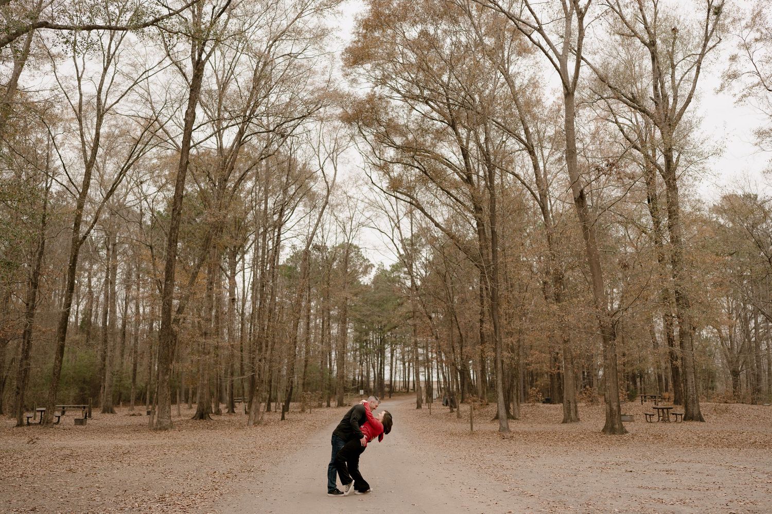 A romantic moment captured in a wooded area with bare winter trees.