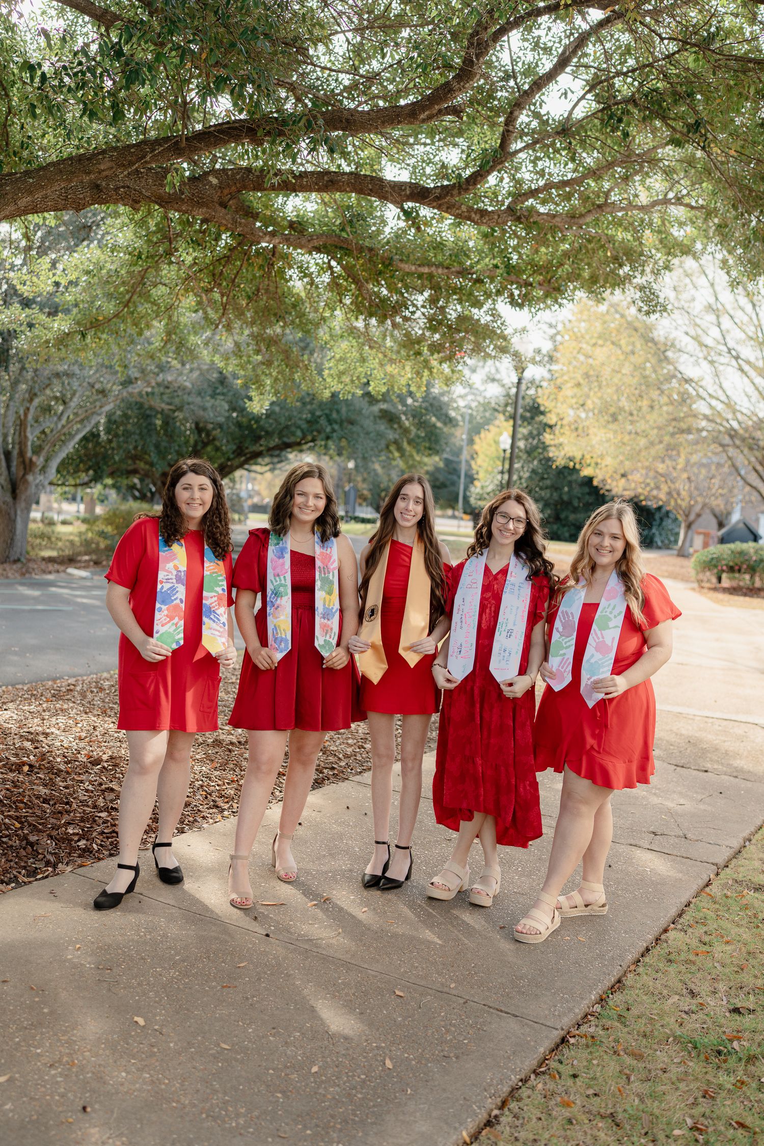 A group in matching red and white outfits poses together outdoors on a tree-lined path.