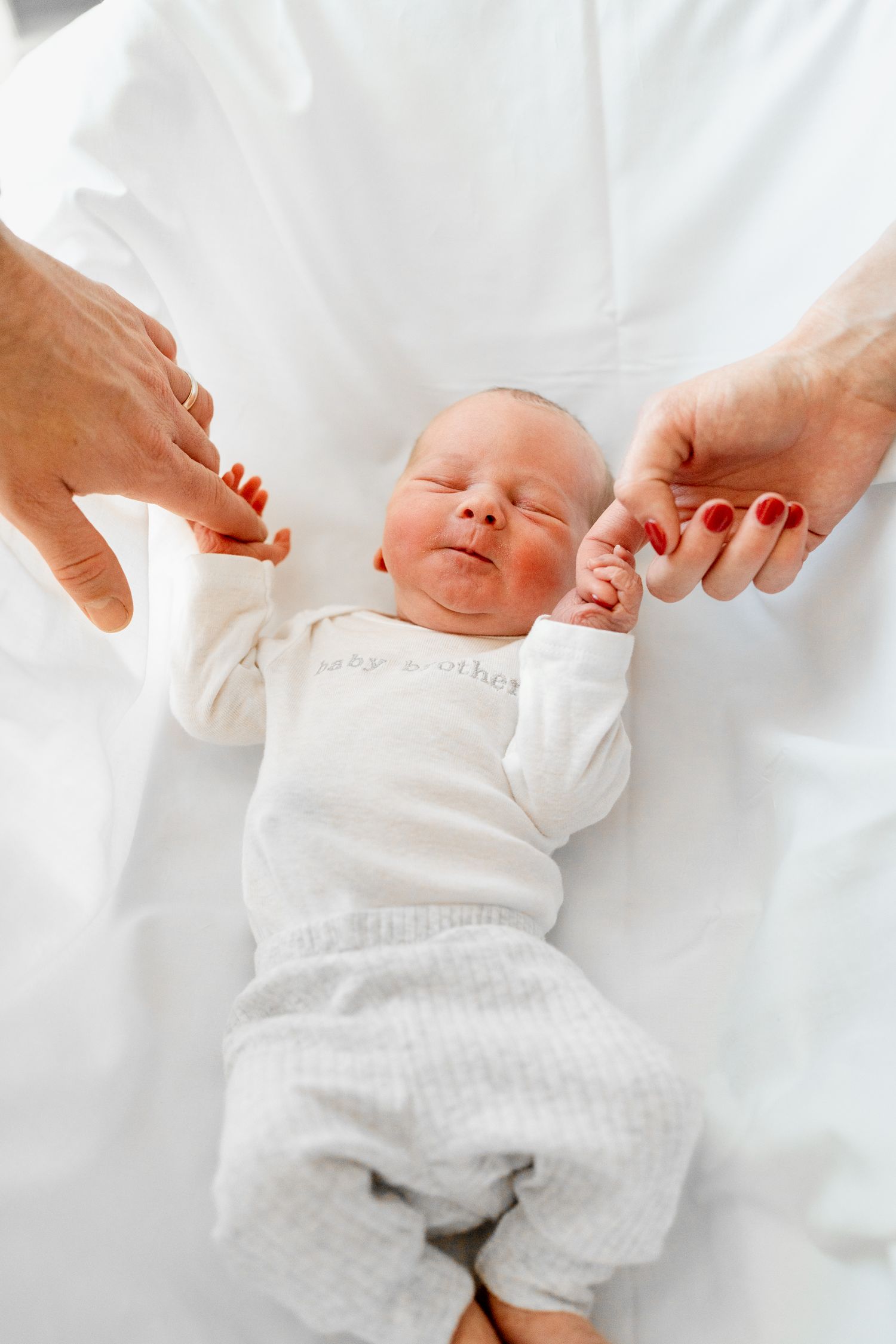 Parents' hands tenderly touching a resting newborn in white clothing.