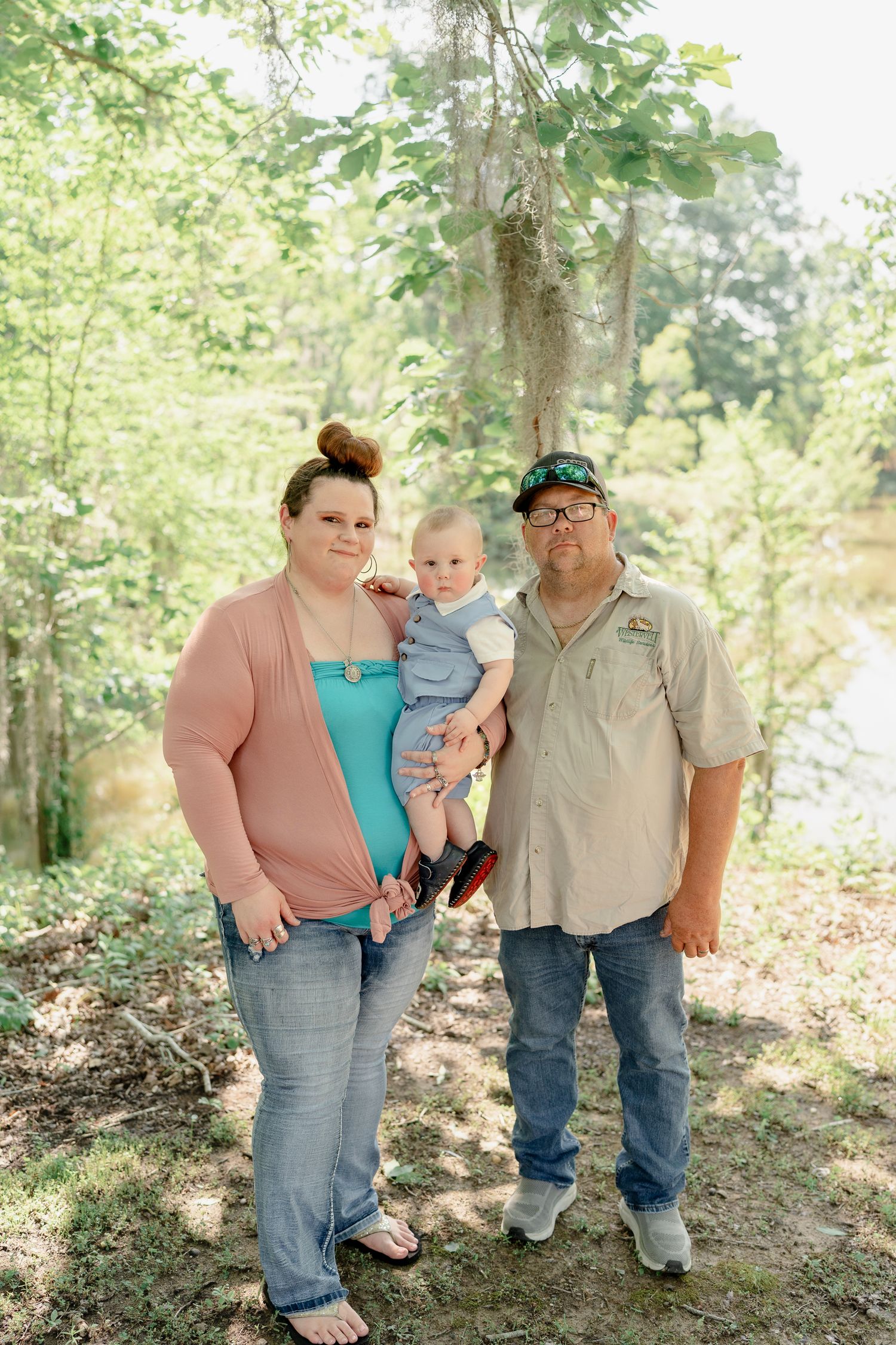 Family group portrait taken in a natural forest setting with dappled sunlight.