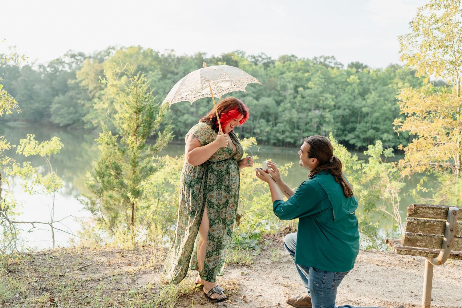 A couple shares a romantic moment under a lace umbrella in an outdoor setting with trees in the background.