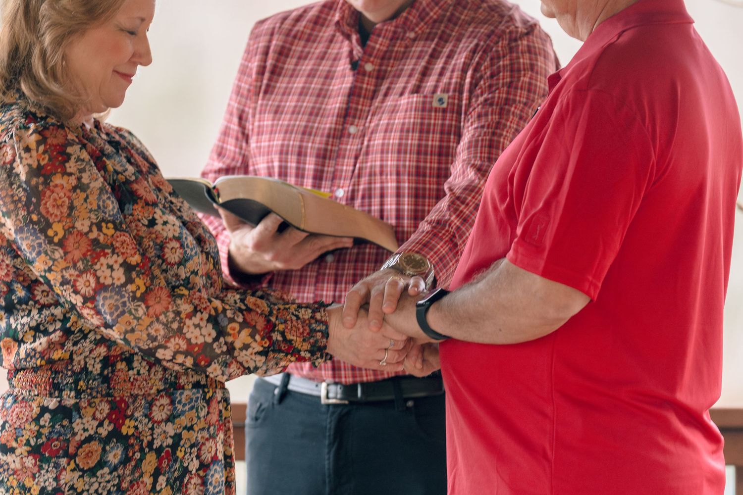 Close-up of couple holding hands with officiant reading from Bible during wedding vows.