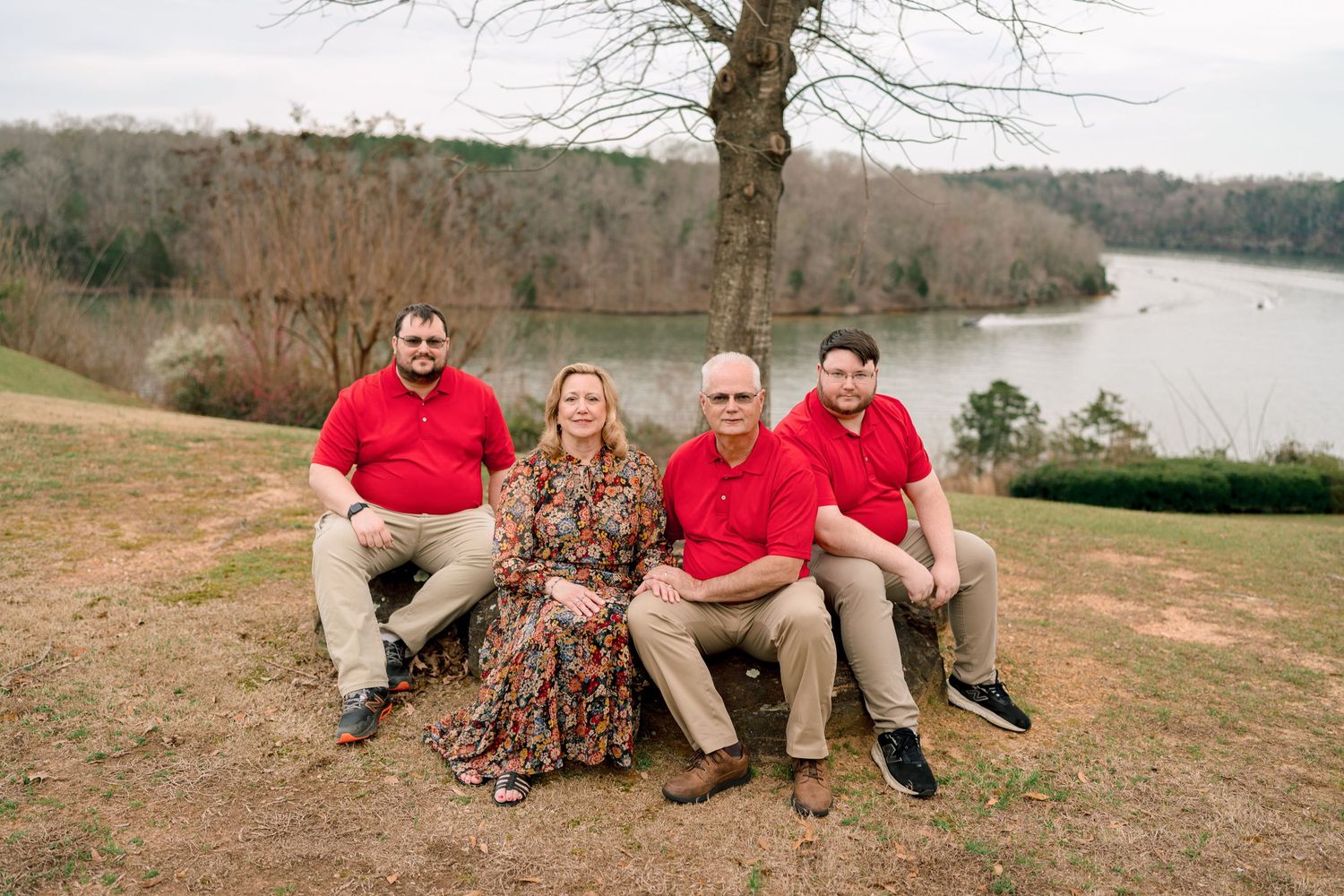 Family of four sitting together on a hillside bench with a peaceful lake view behind them.