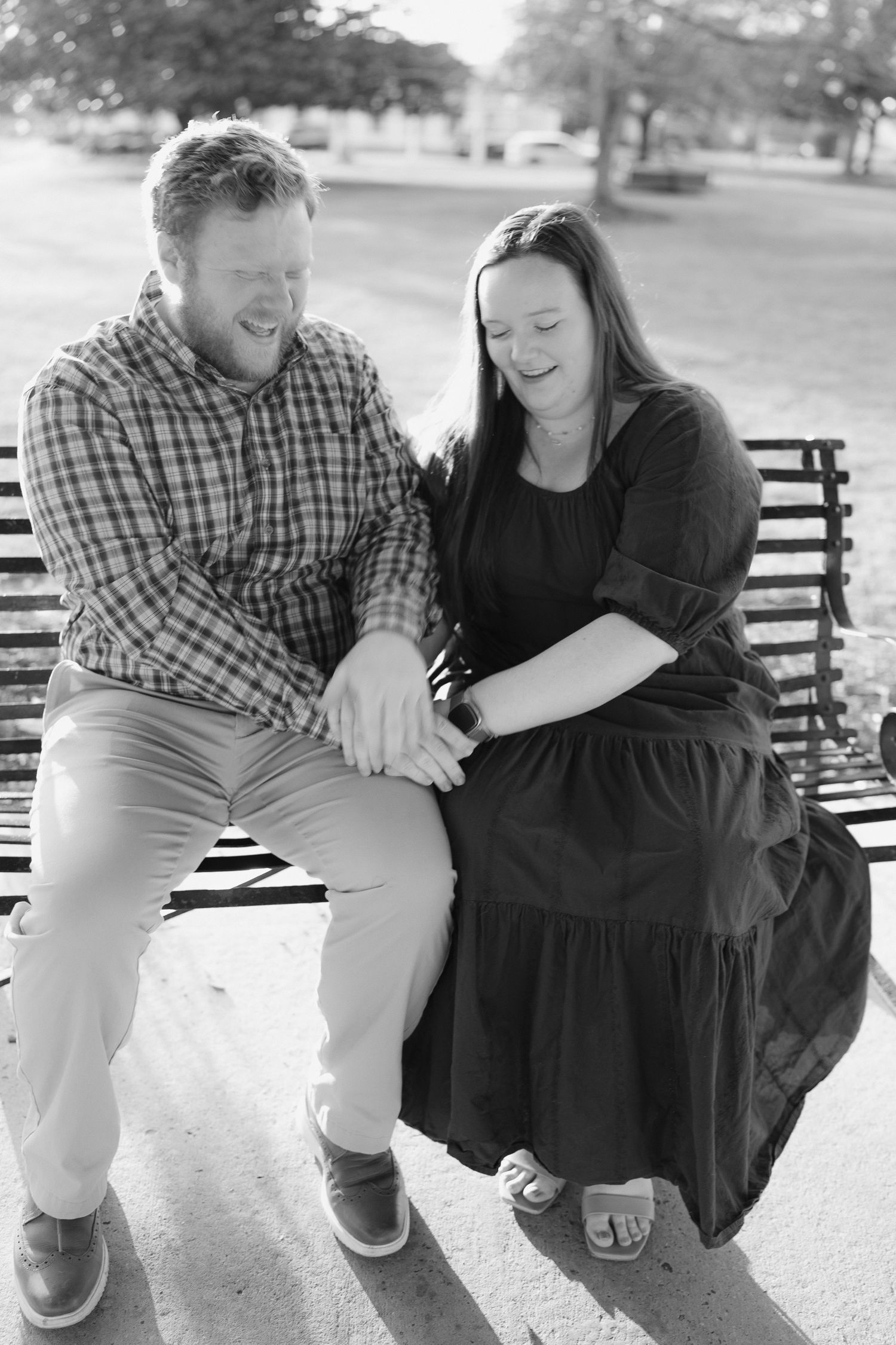 Black and white photo of laughing couple sitting close together on a sunny park bench.