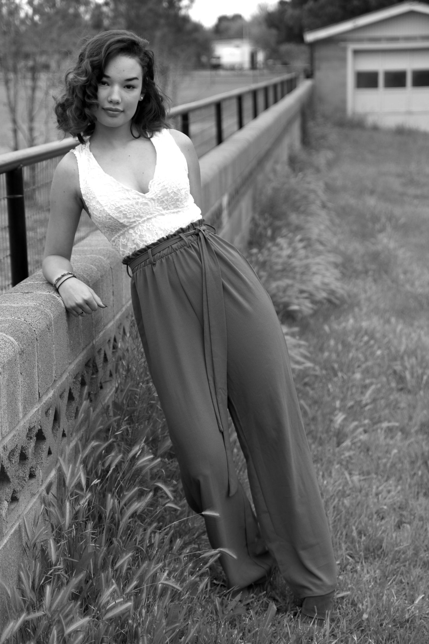 Woman in white top and olive pants poses against concrete wall in black and white photo.