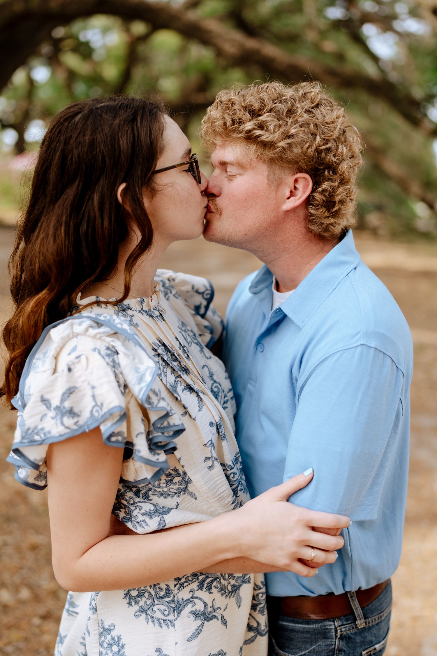 Intimate couple sharing tender kisses under oak trees wearing coordinated casual outfits.