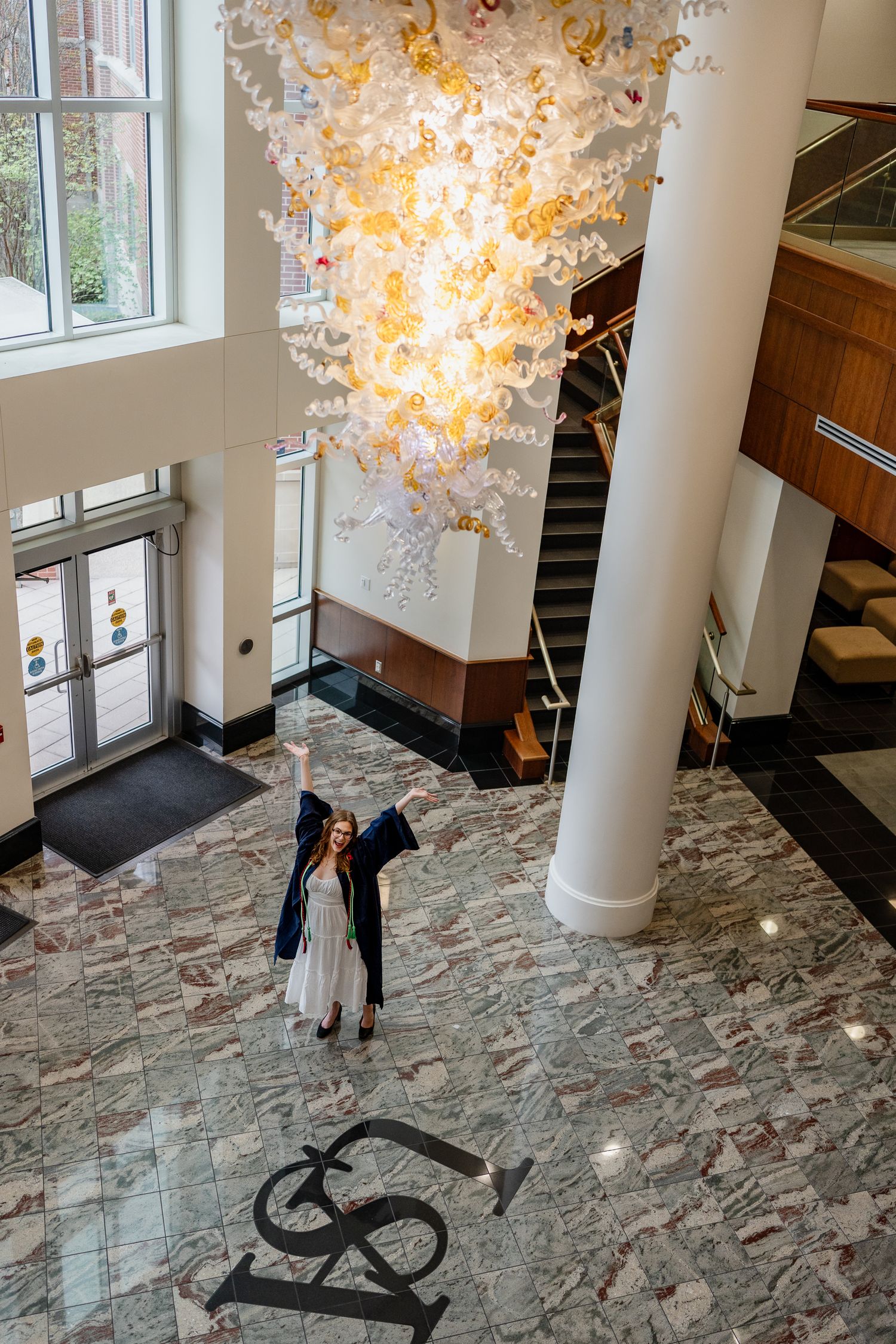 Elegant chandelier hanging above marble floors and white columns in a grand lobby.