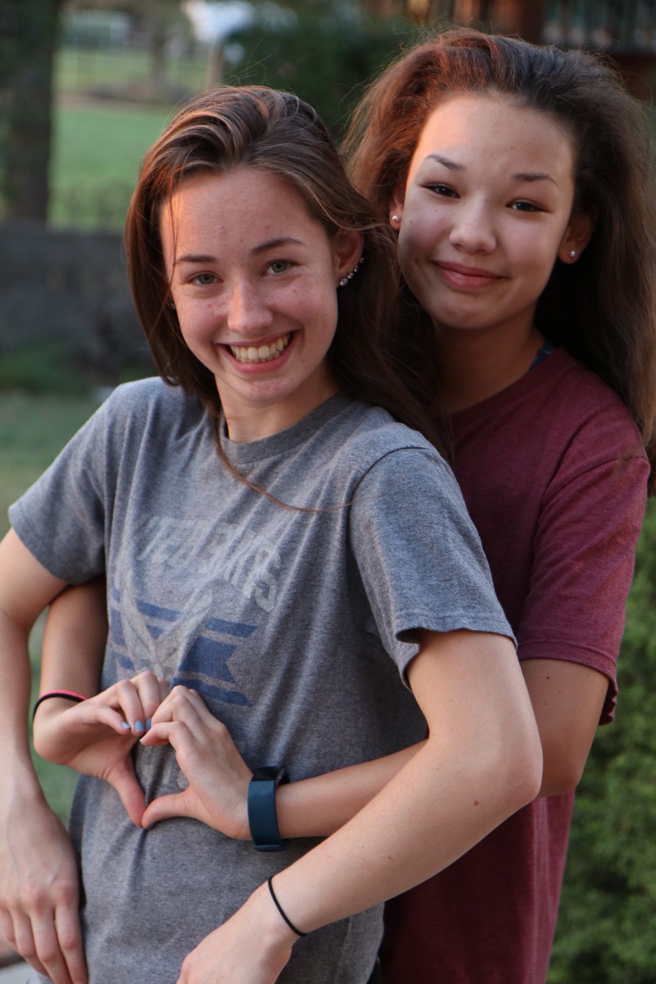 Two friends pose together making a heart shape with their hands.